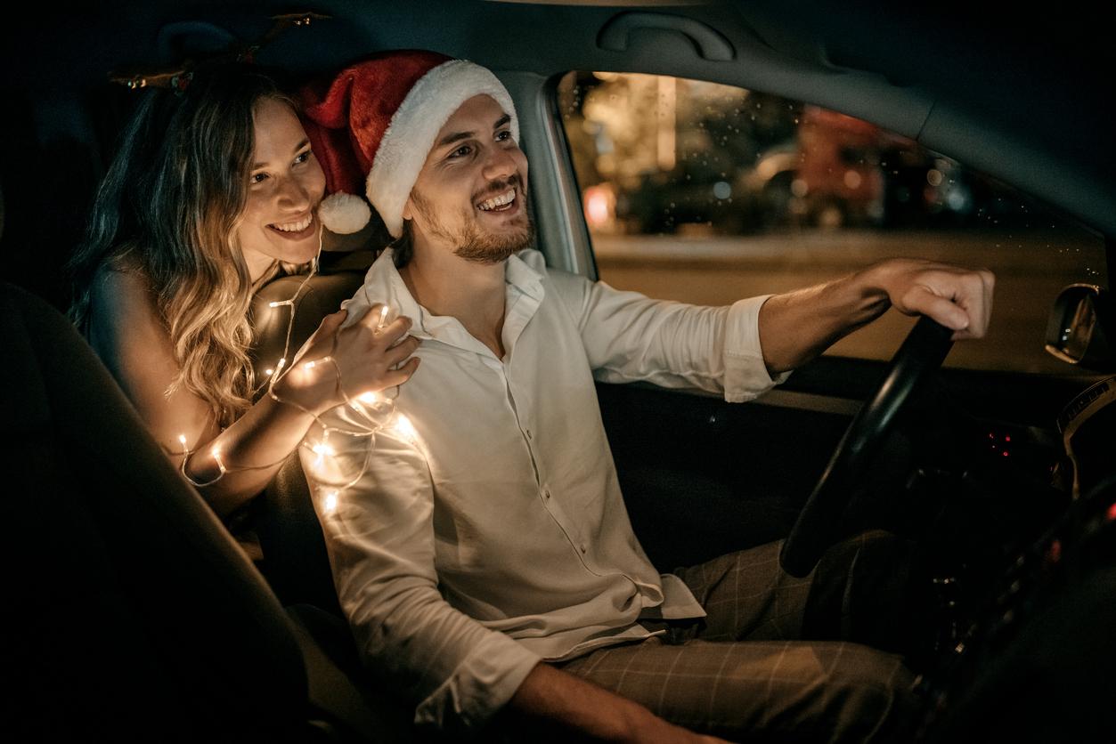 A man and a woman sitting in a car with festive lights and a santa hat