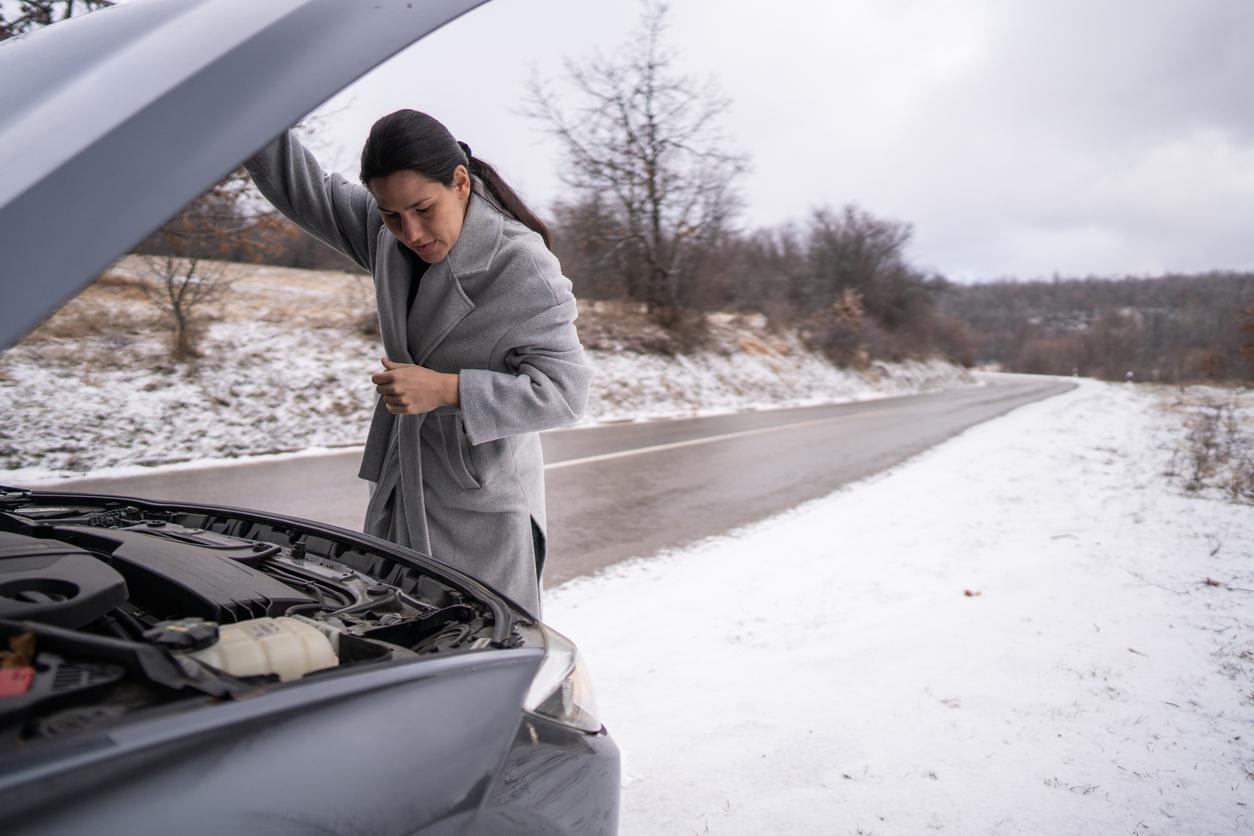 A women inspecting a car engine in the snow