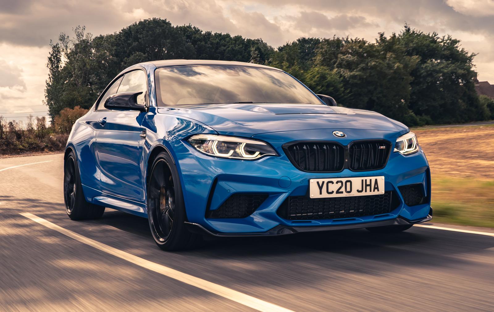 a blue bmw m2 with black wheels driving on a windy road 