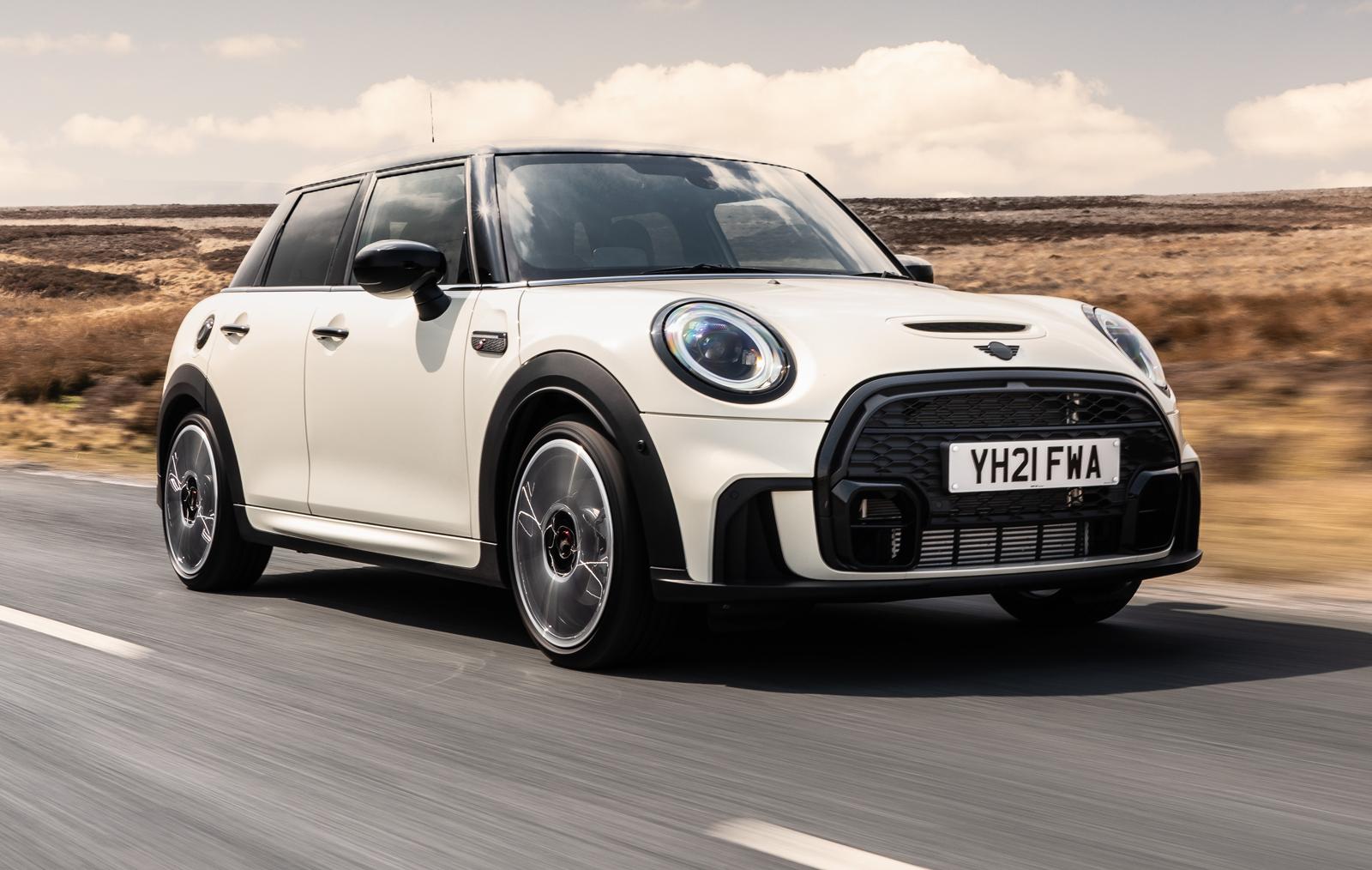 a white mini cooper hatchback driving on a country road