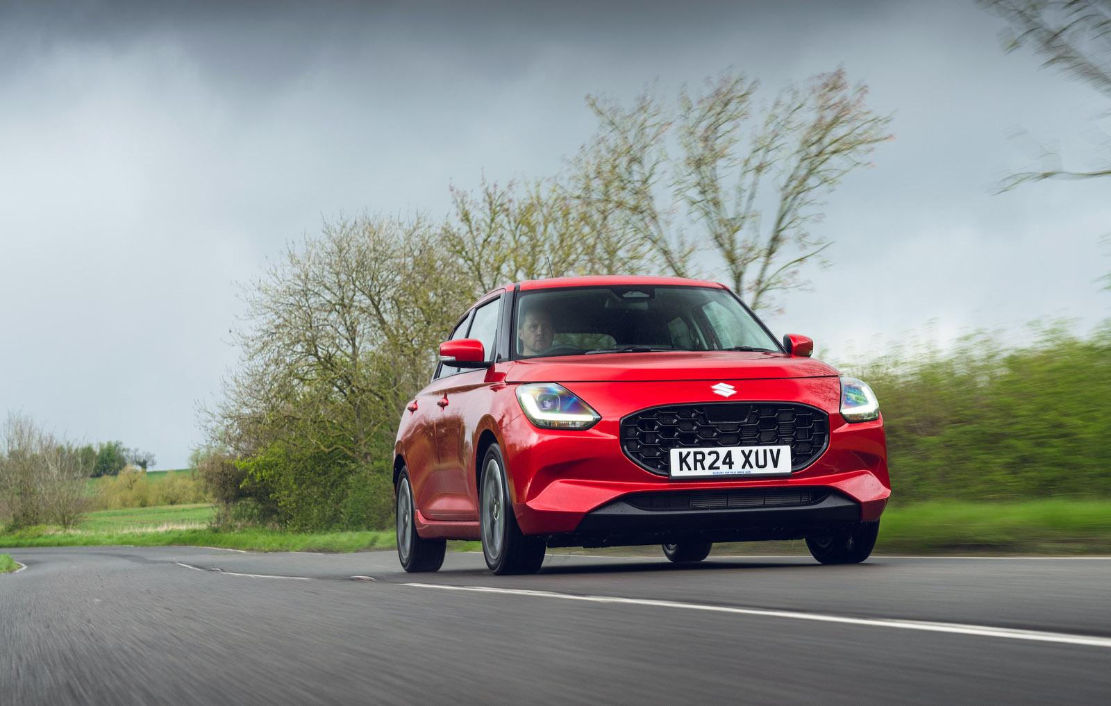 a red suzuki swift hybrid driving on a country road