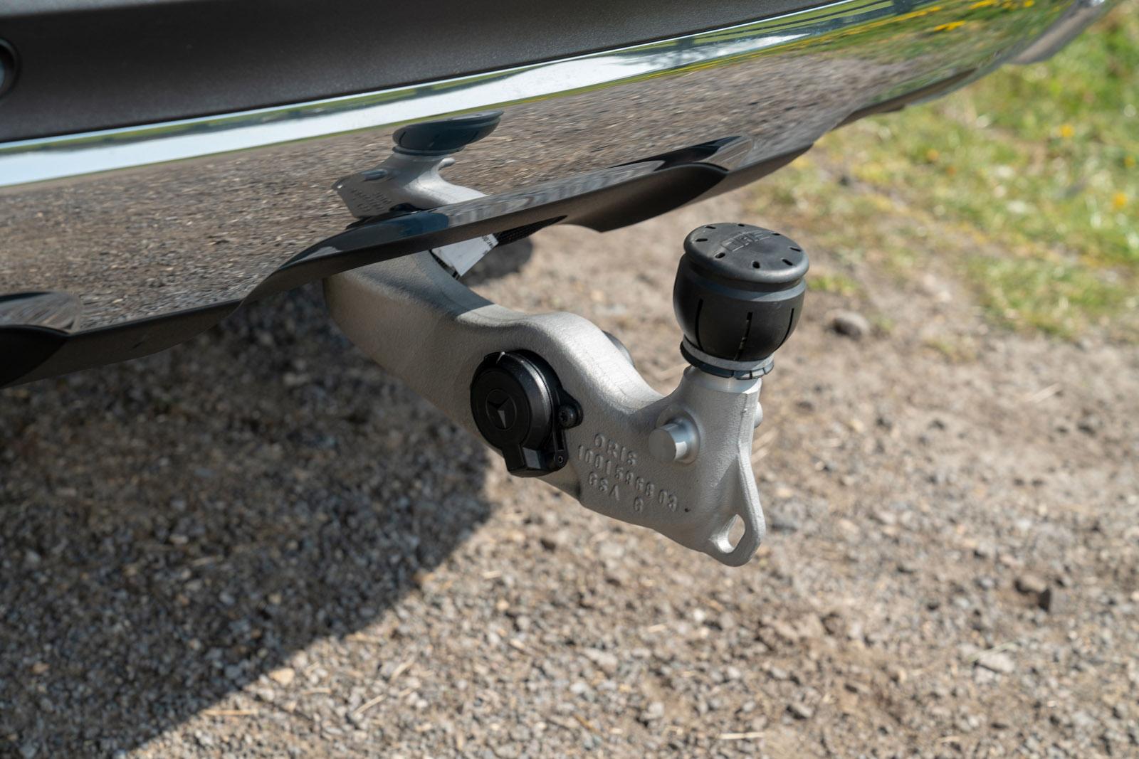 Close-up of a car's tow hitch with a detachable tow ball, mounted on a metallic bracket, parked on a gravel surface.