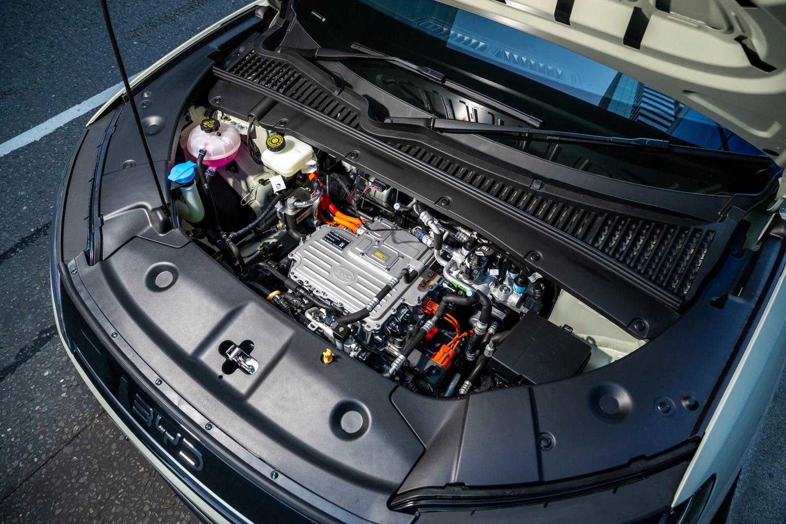 Close-up of a car engine compartment with various components visible, including coolant reservoirs, wires, and a central engine unit.