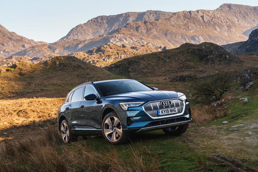 Blue Audi SUV parked on a grassy hill with rugged mountains in the background under a clear sky.