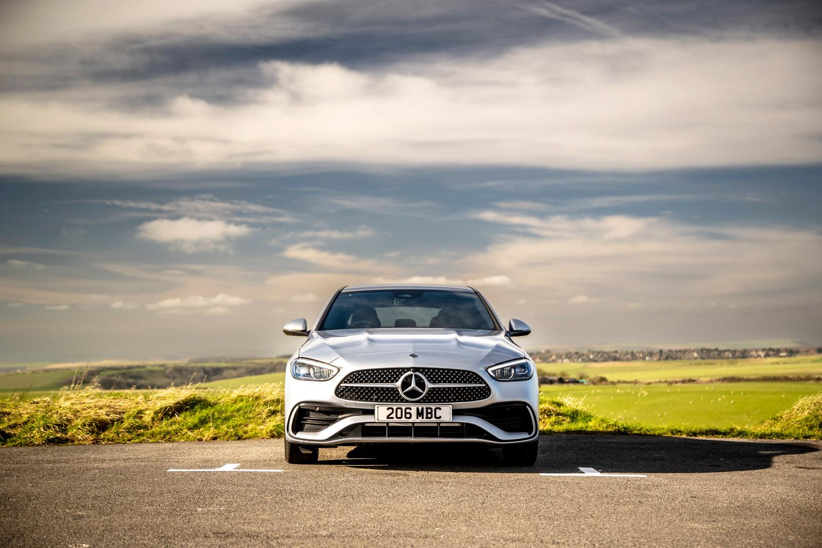 Silver Mercedes-Benz car parked on a scenic road with a cloudy sky and greenery in the background.