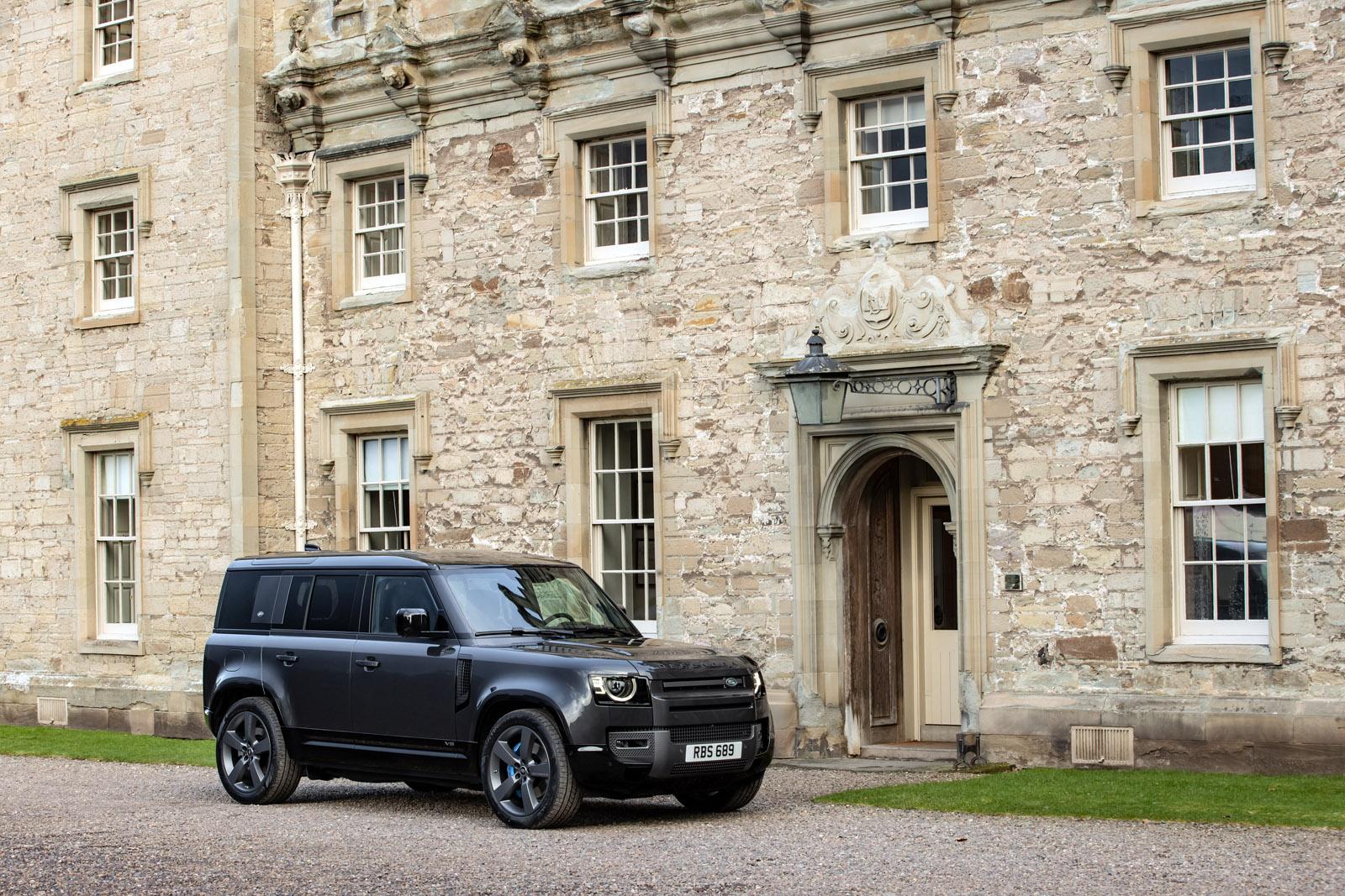 Black Land Rover Defender V8 next to a stone building