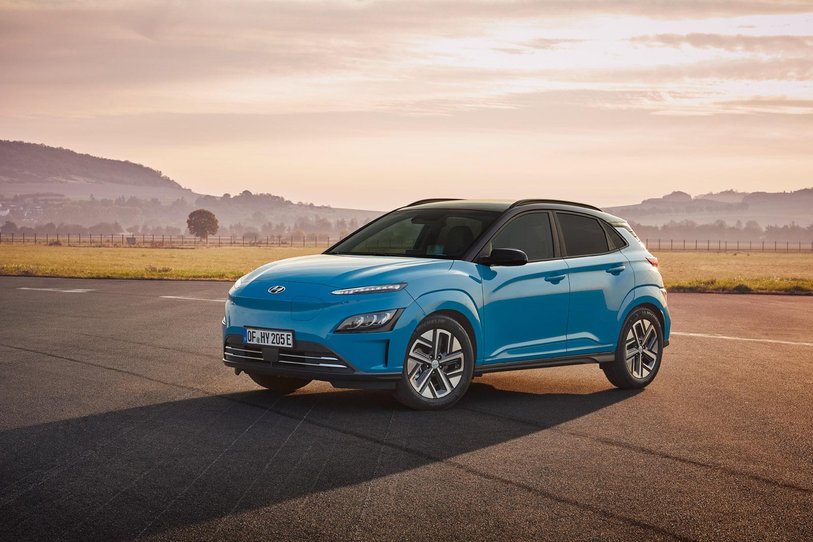 Blue SUV parked on a paved road with mountains and a hazy sky in the background at sunrise or sunset.