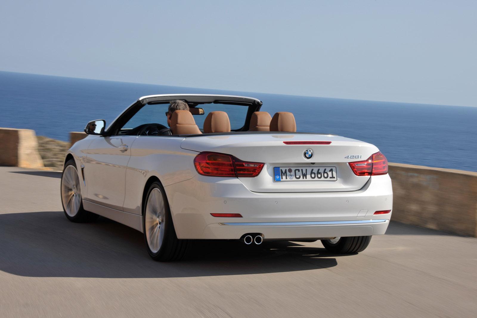 White convertible driving on a coastal road, top down, with a view of the sea and clear sky in the background.
