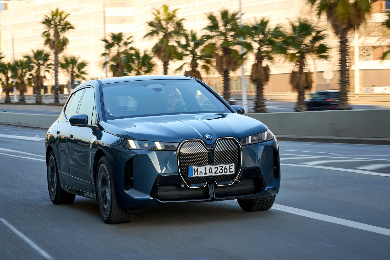 A blue BMW SUV driving on a city road lined with palm trees, under a clear sky.