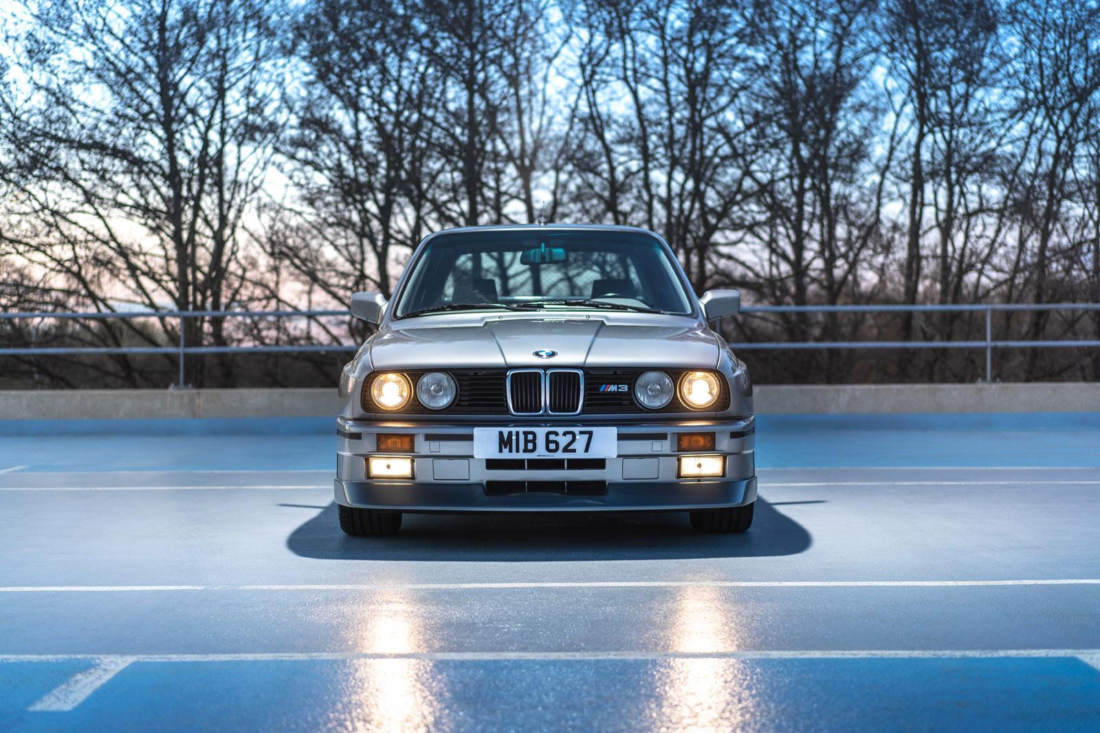 a silver BMW E30 M3 front with headlights on