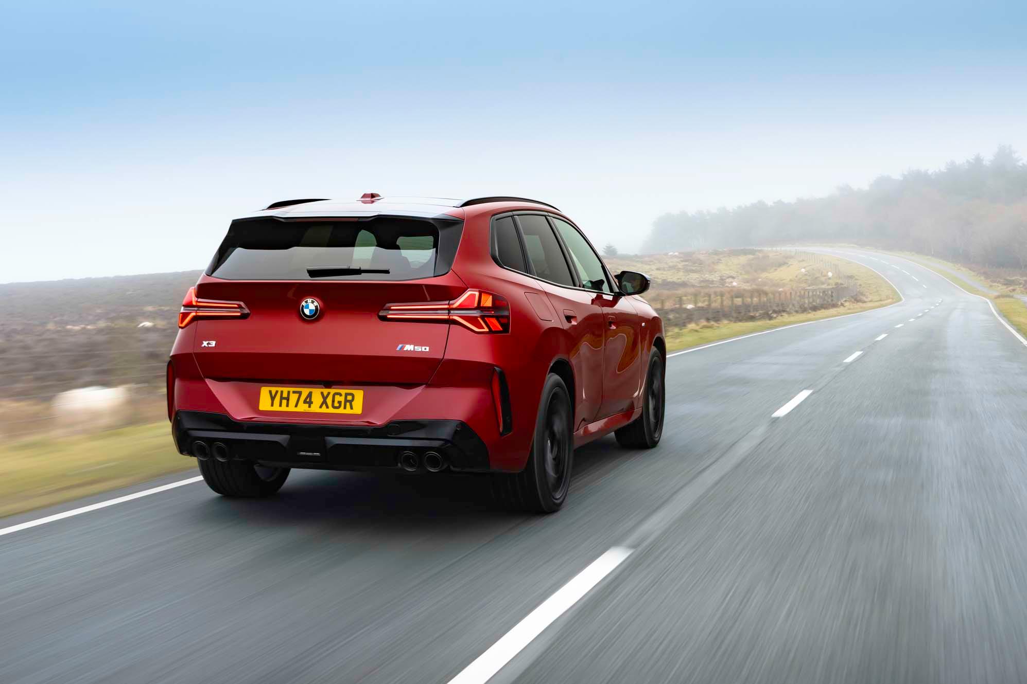 Red SUV driving on an empty, winding road through a misty landscape, with trees and fields in the background.