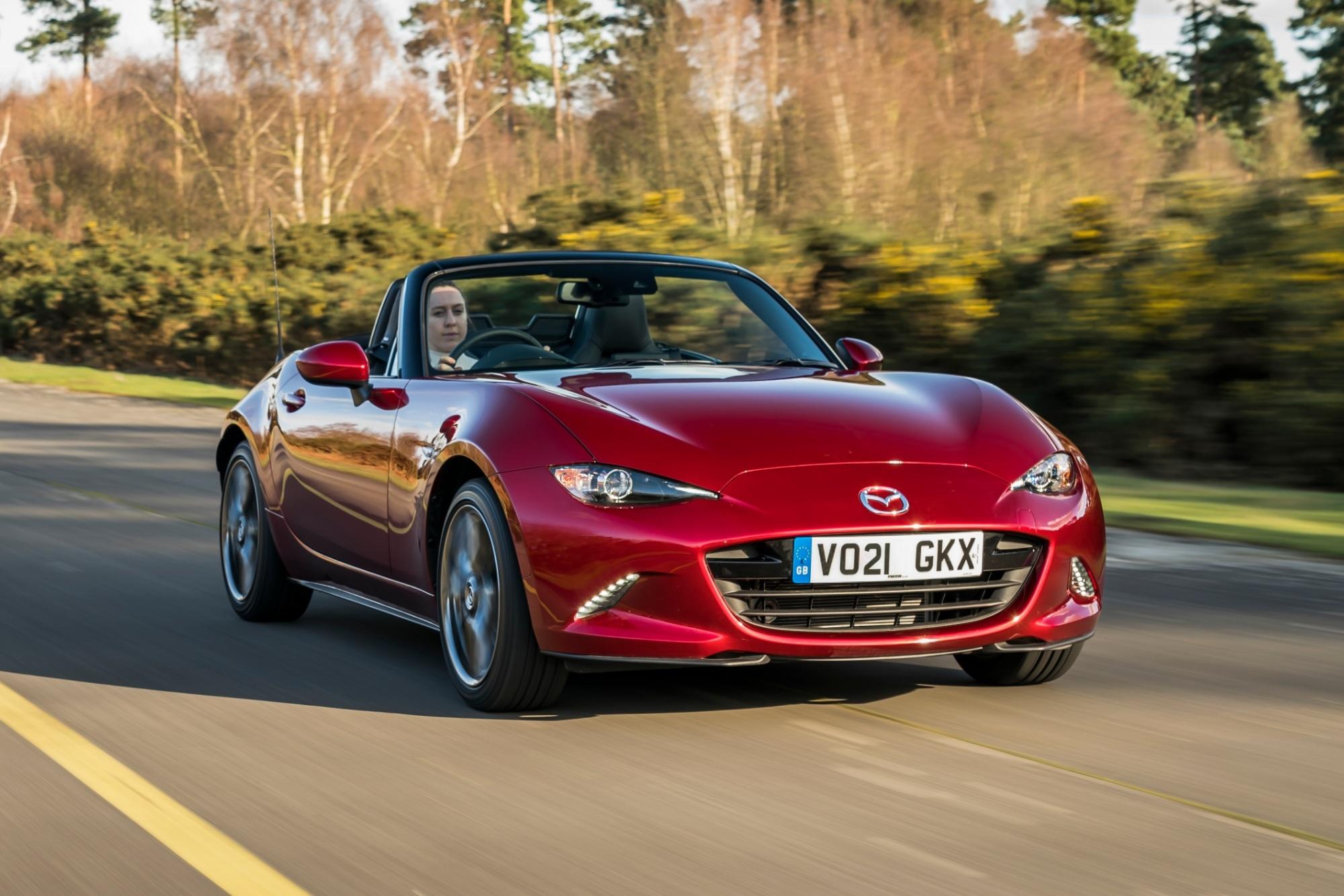 a red mazda mx-5 driving on a country road