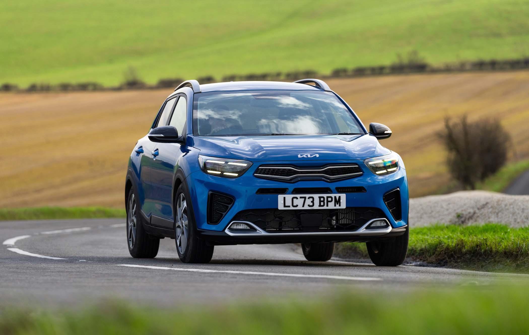 Blue Kia Stonic driving on a winding country road with green and brown fields in the background.