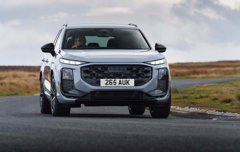 Silver Audi Q3 driving on a country road, with overcast skies and grassy fields in the background.