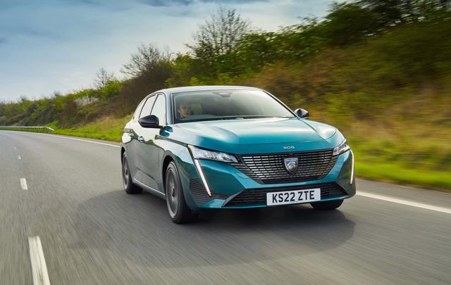 A teal Peugeot 308 SW drives on a highway surrounded by greenery under a clear sky.