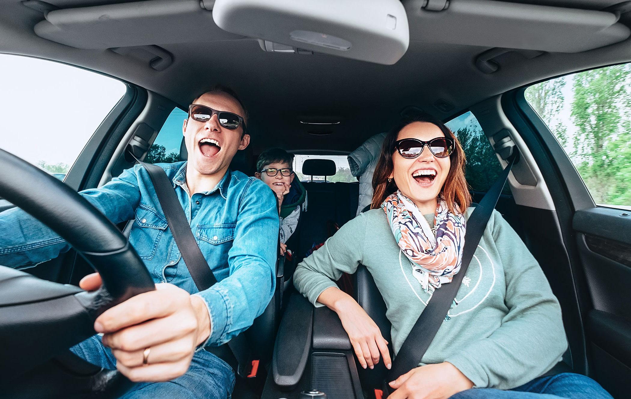 Two happy adults sat in the front of a car, with a child in the back