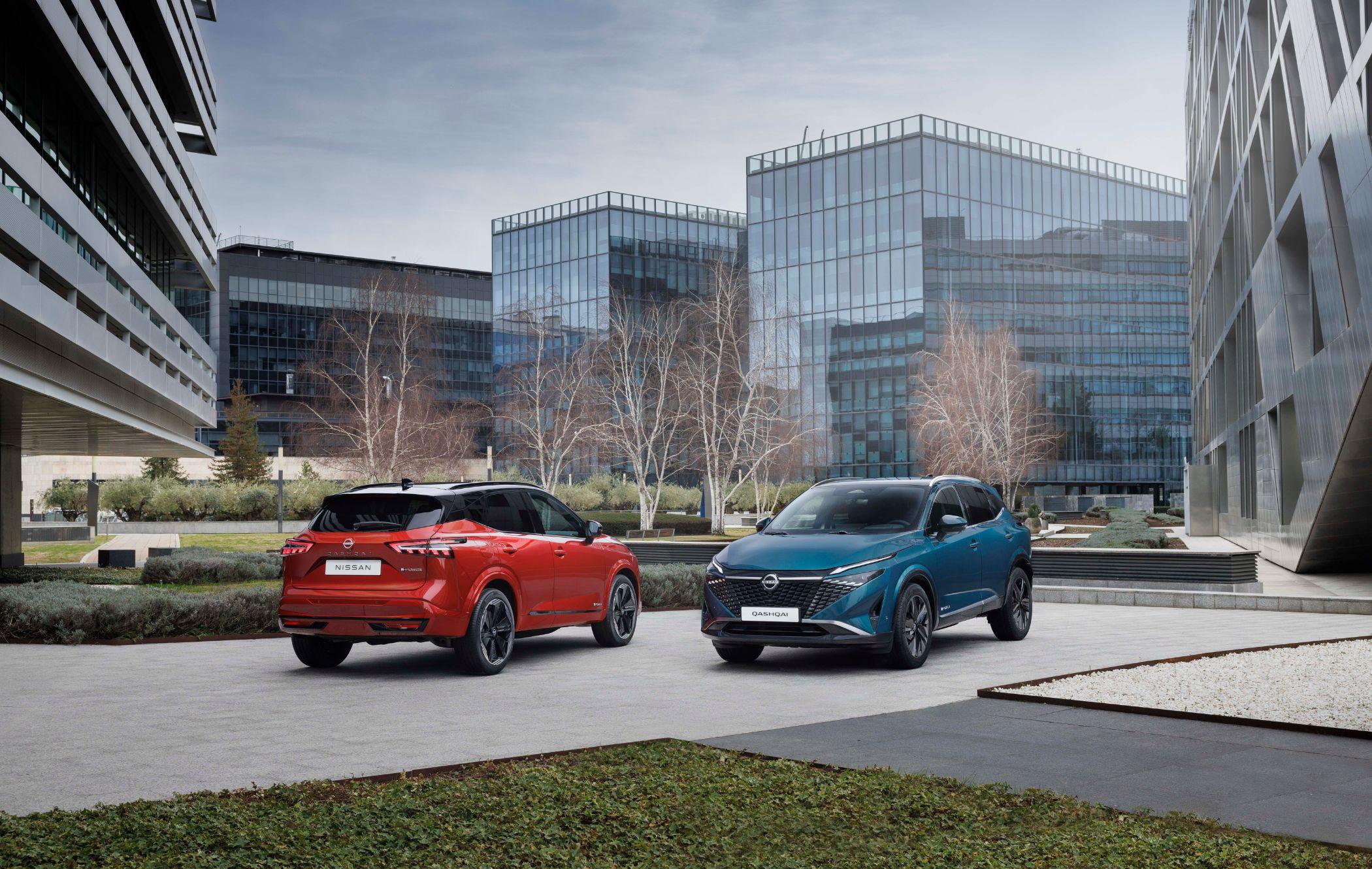 Two Nissan Qashqais parked on a city street, surrounded by glass buildings and bare trees on a cloudy day.