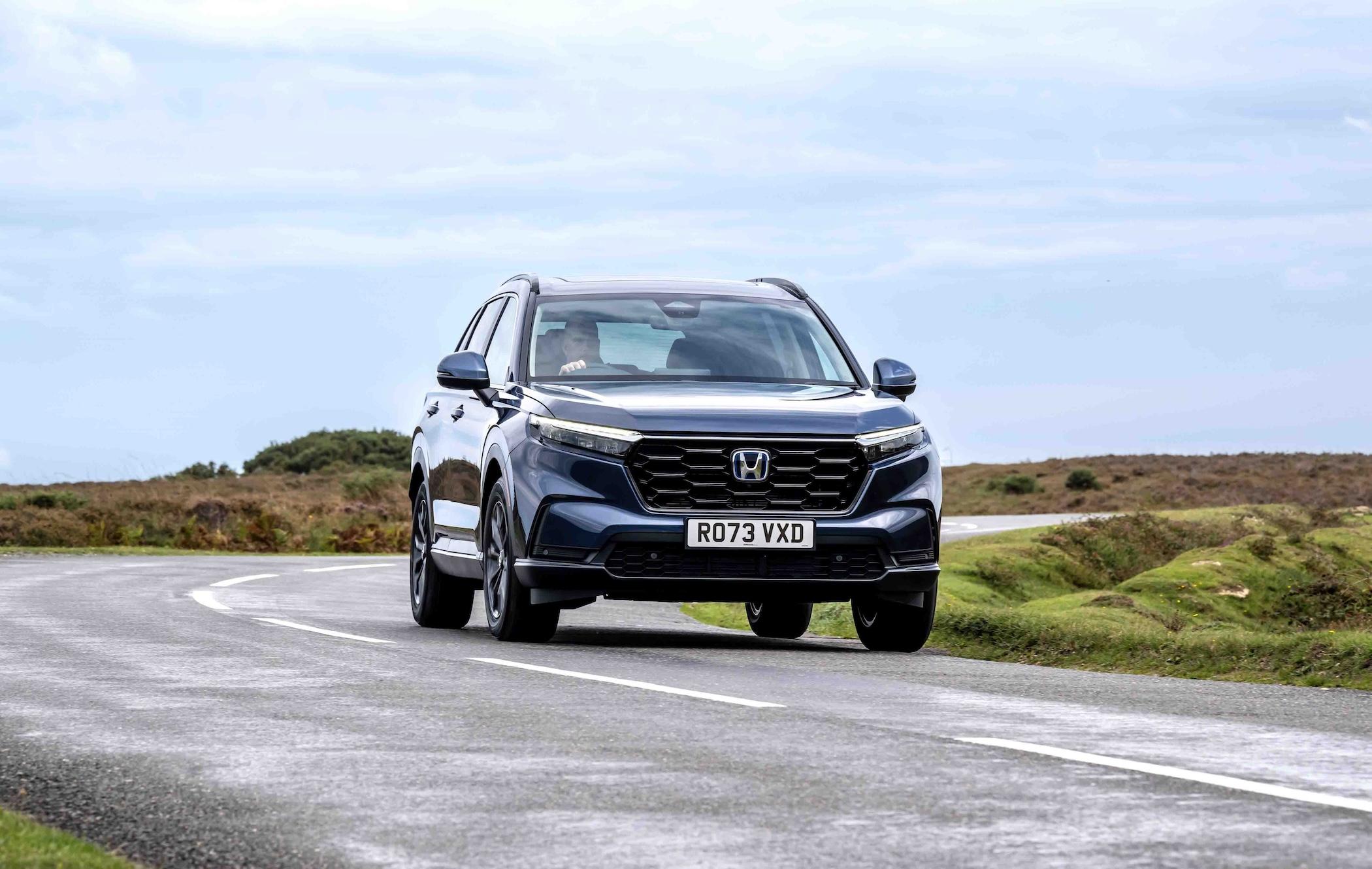A blue Honda CR-V drives on a winding road through a scenic landscape with cloudy skies.
