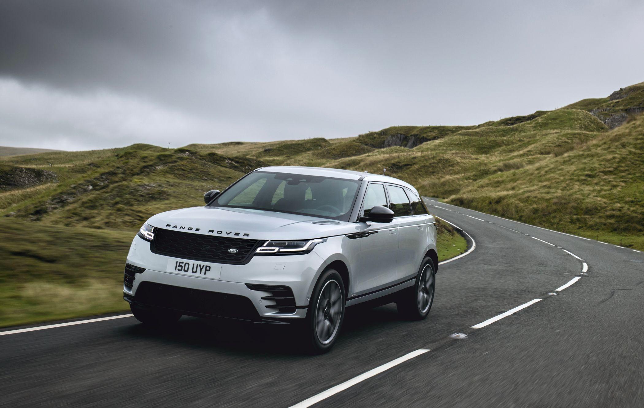 Silver Range Rover Velar driving on a winding road through a hilly landscape under a cloudy sky.