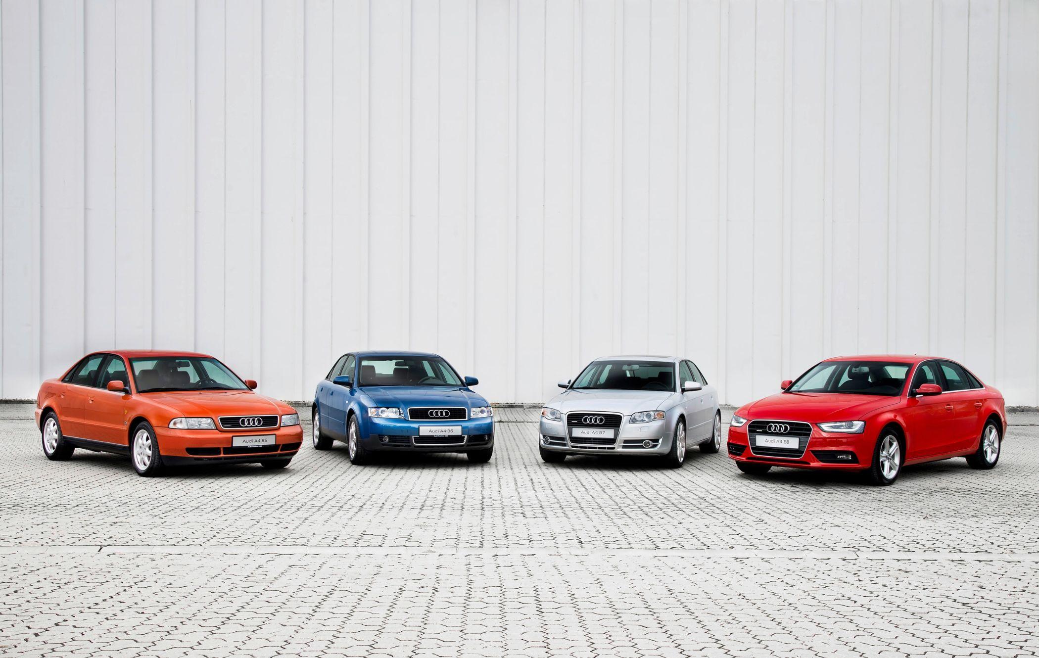 Four Audi A4 saloons in different colors—orange, blue, silver, and red—parked on a paved surface against a white wall.