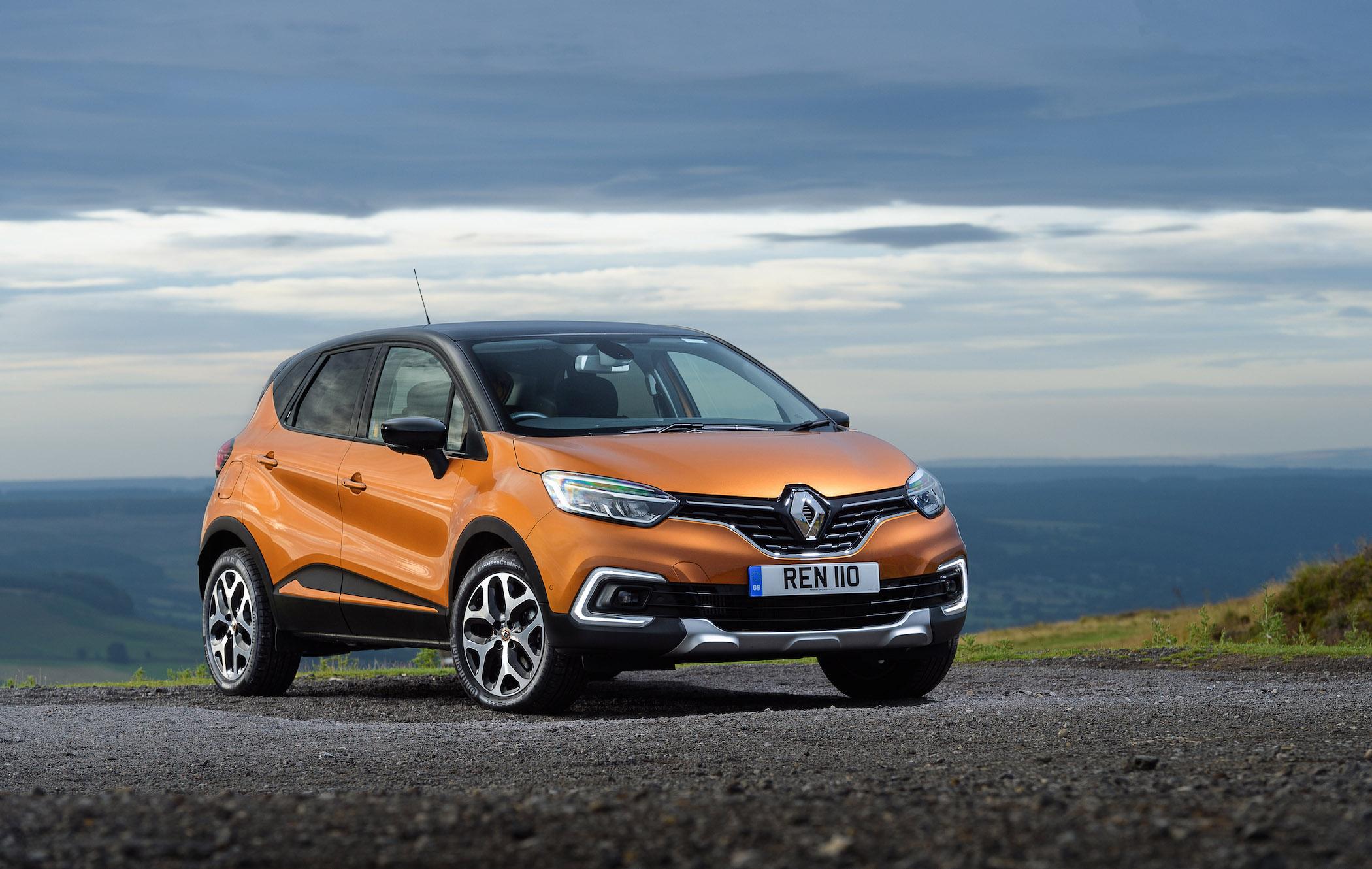 an orange renault captur parked on gravel in front of a valley