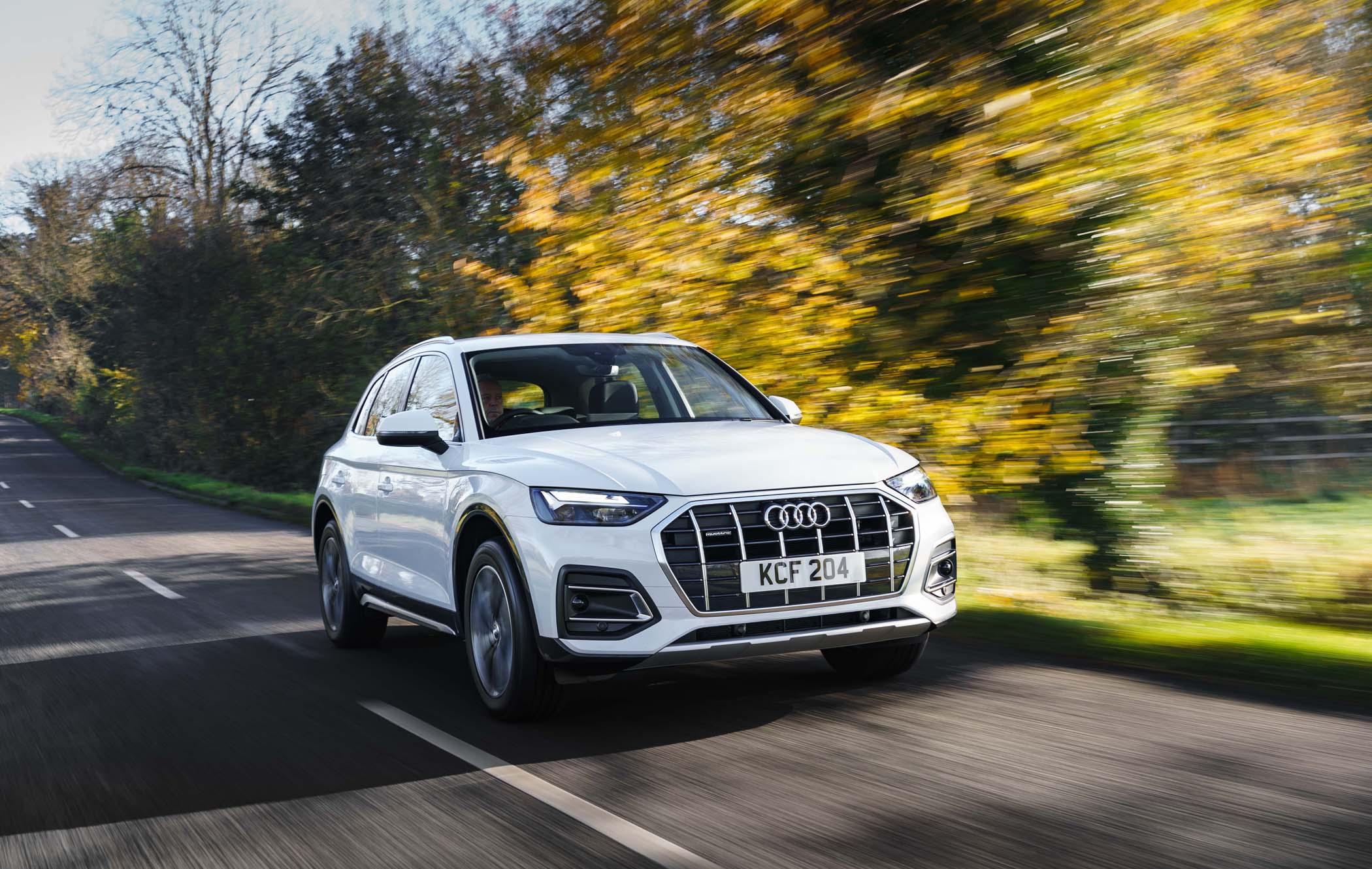White Audi Q5 driving on a countryside road with blurred autumn trees in the background.