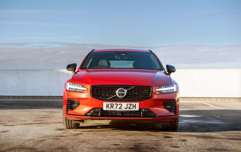 Red Volvo V60 parked in an open area, viewed from the front, under a clear blue sky.