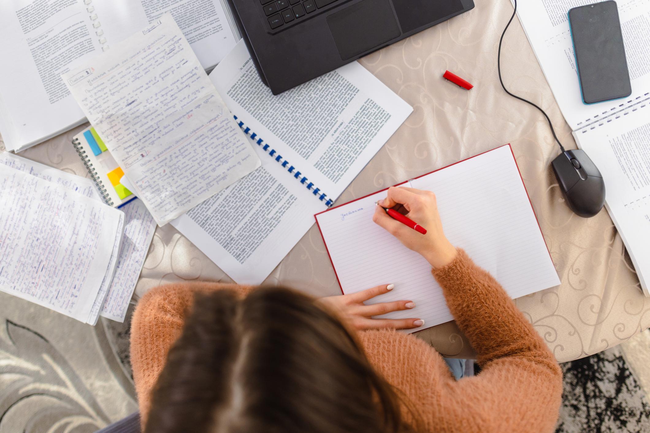 A girl revising at a desk surrounded by books and a laptop