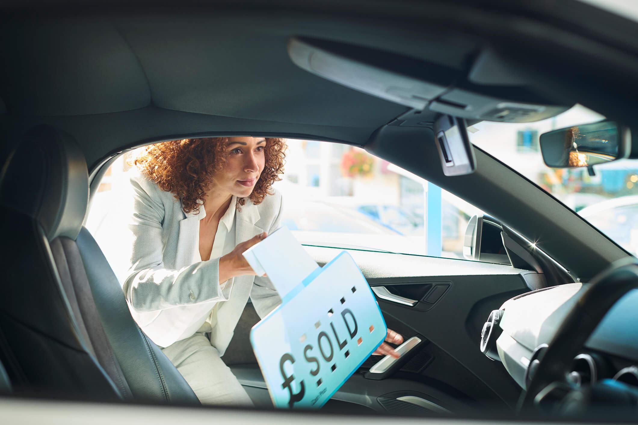 A woman putting a 'sold' sign in a car