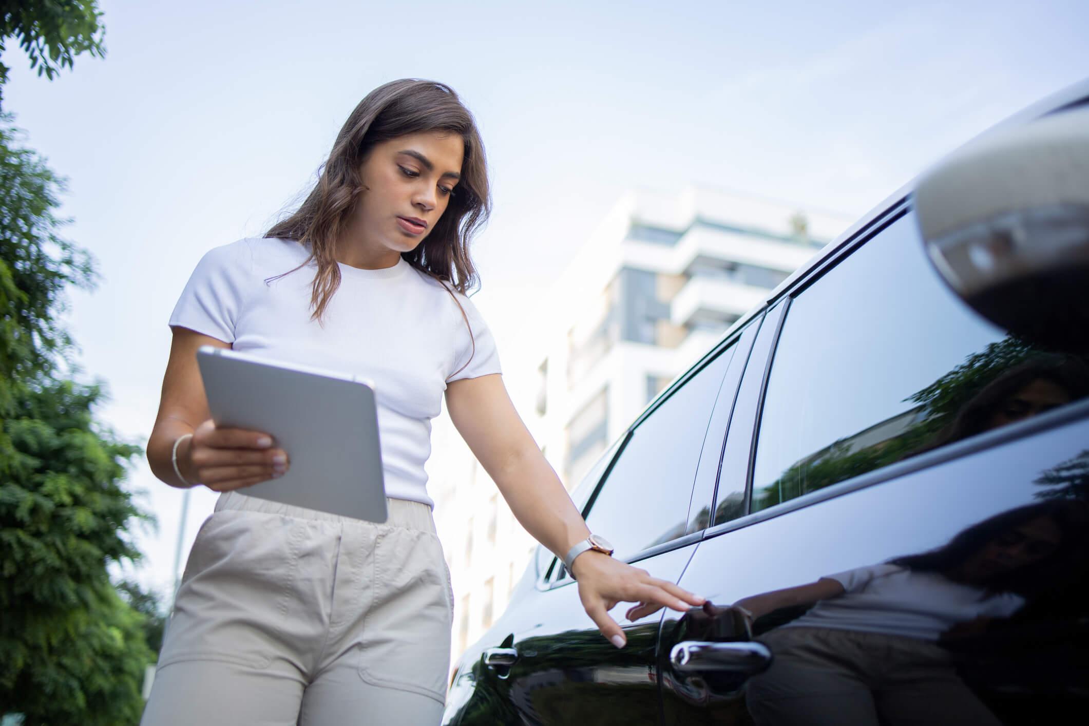 A woman checking the side of a car with an ipad in hand