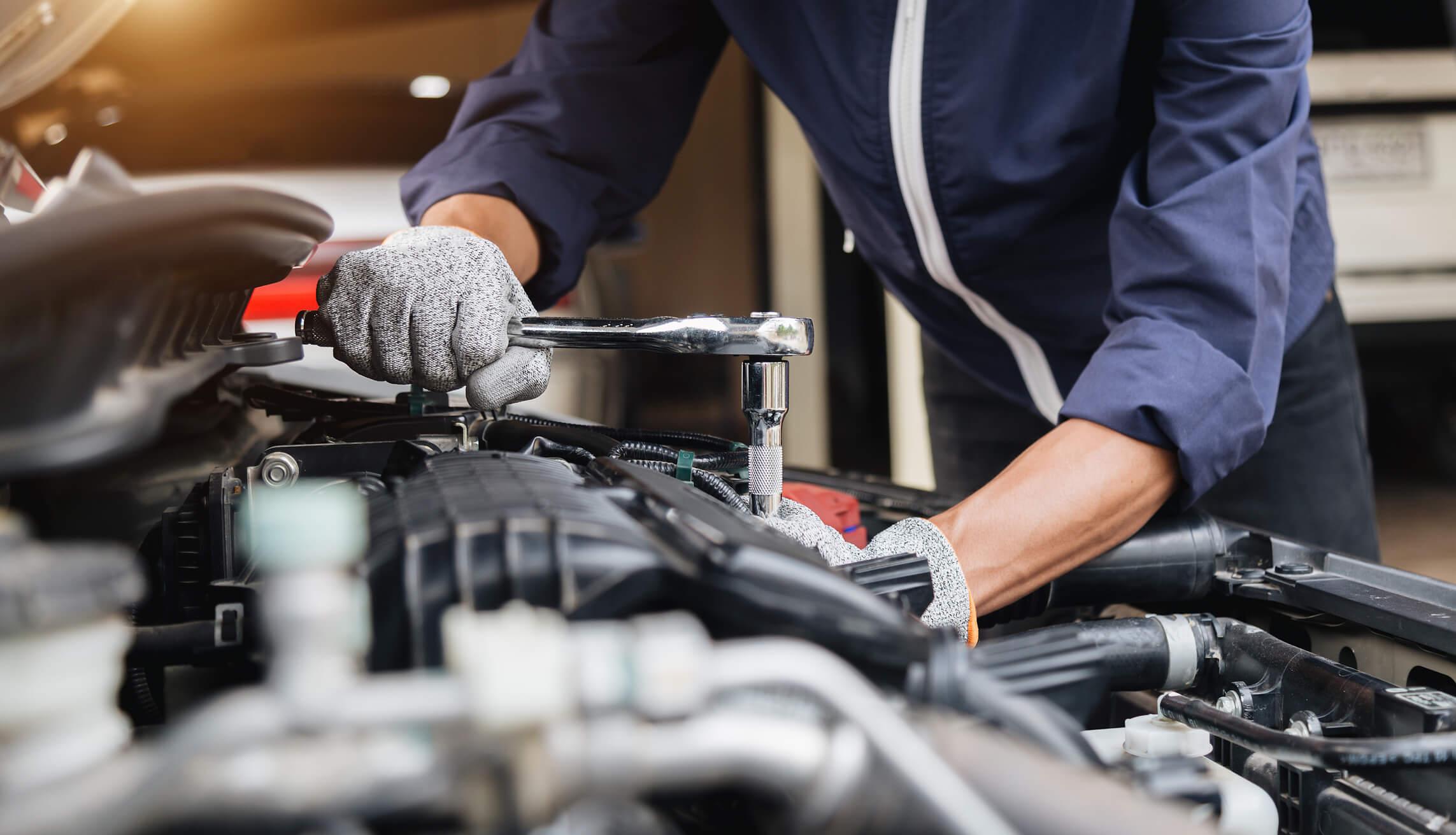 Hands using a tool in the bonnet of a car