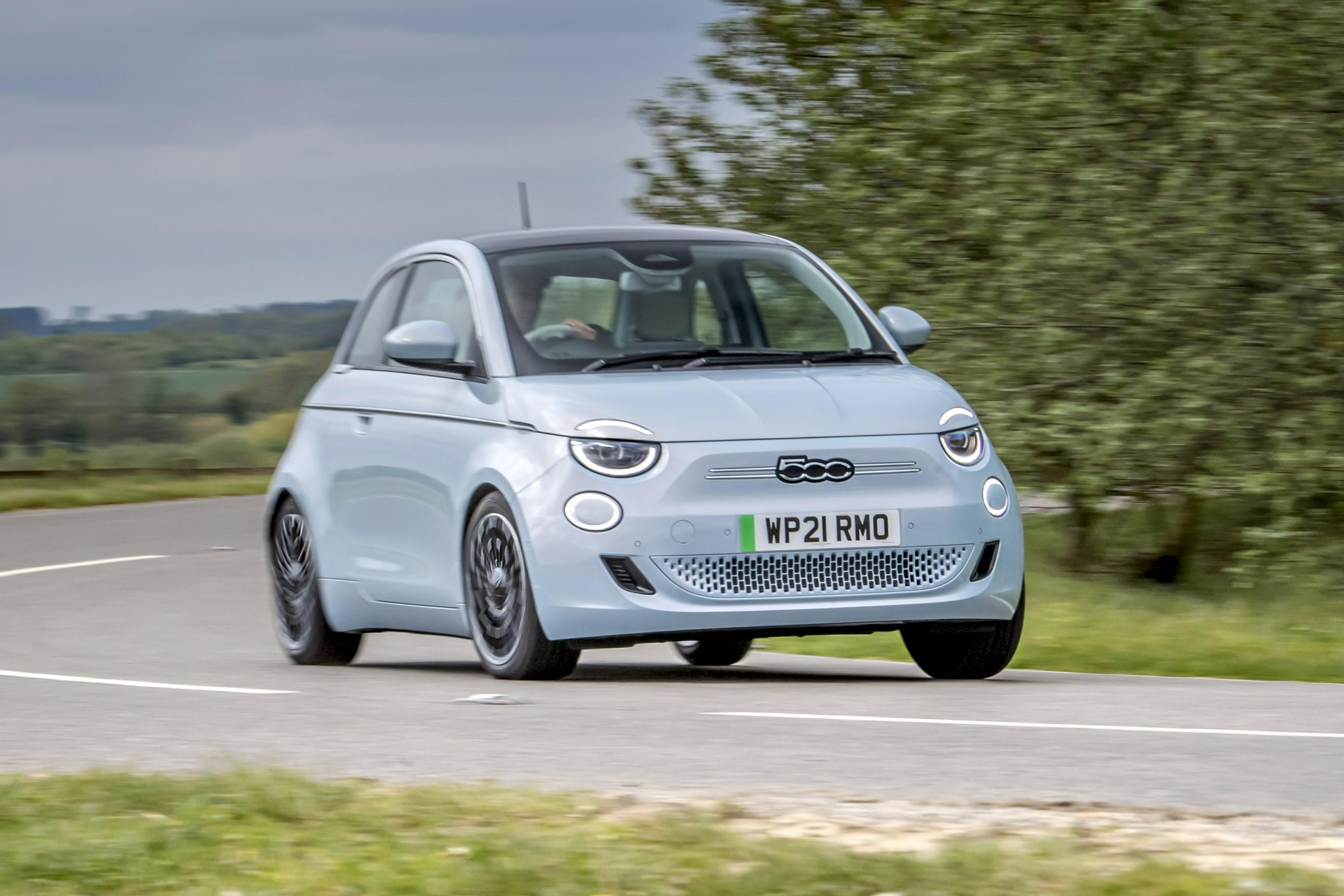 A pastel blue Fiat 500 electric driving on a country road