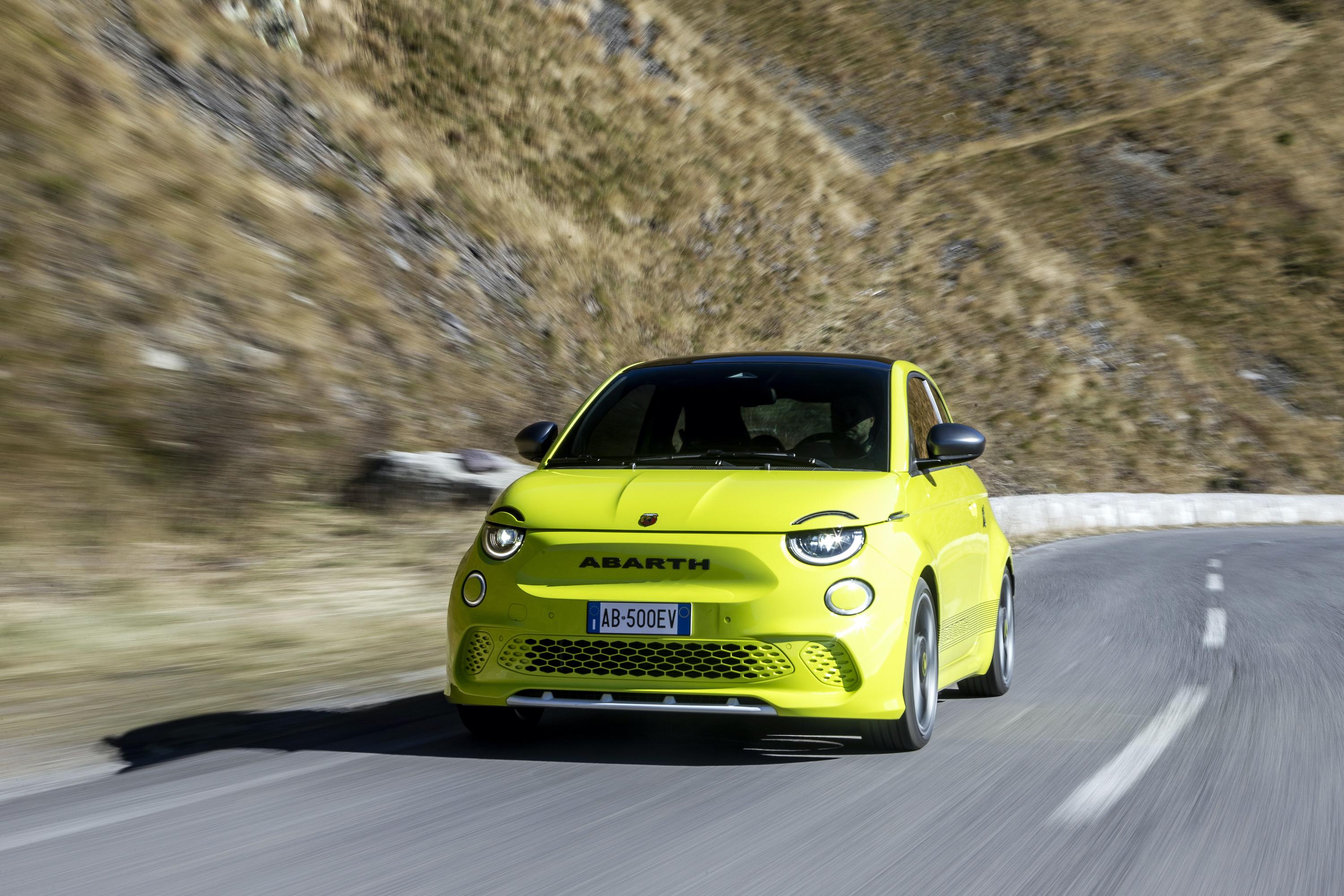 bright yellow abarth 500e driving on a mountain road in the sun