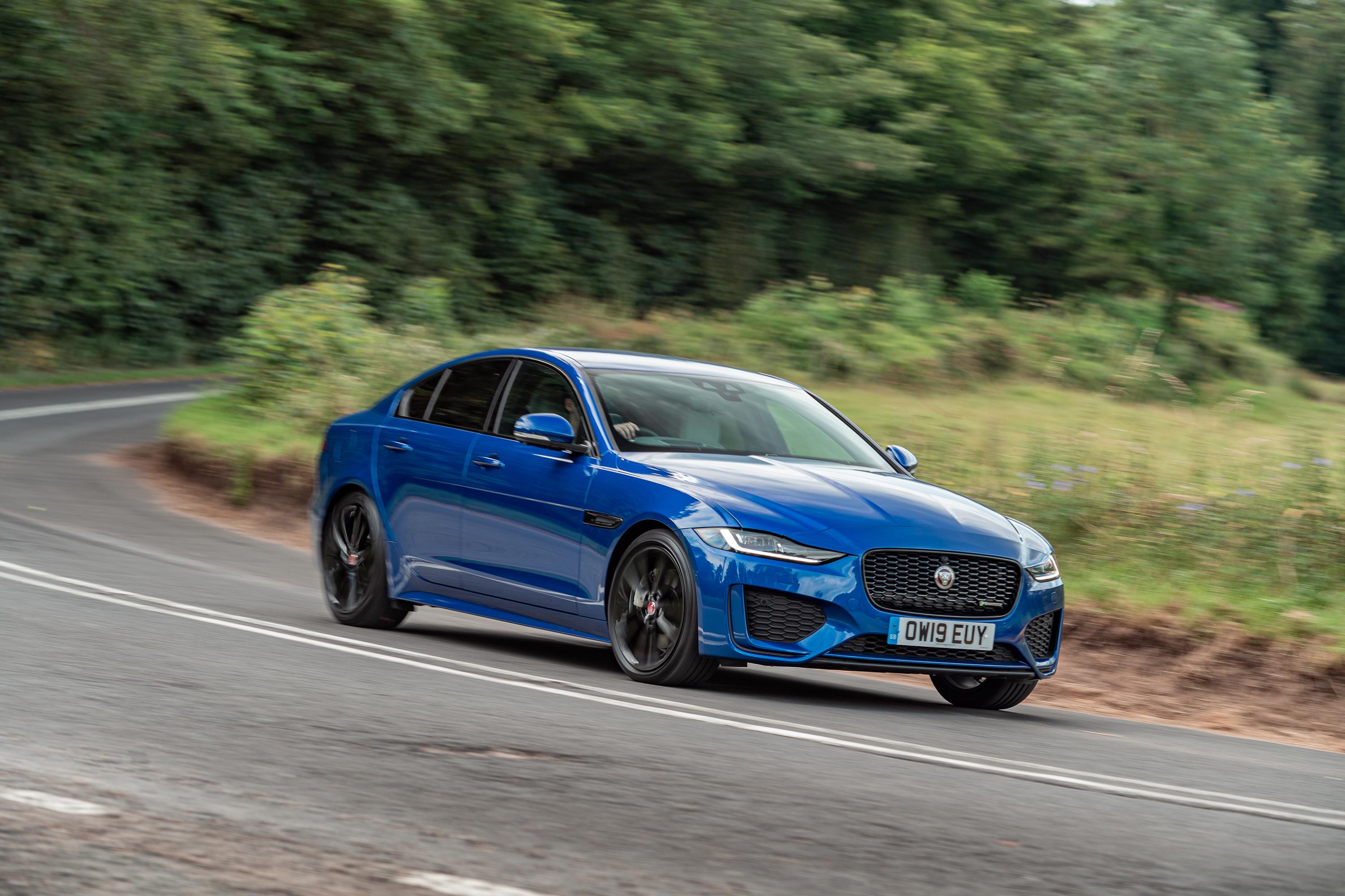 a dark blue jaguar xe with black wheels driving on a road