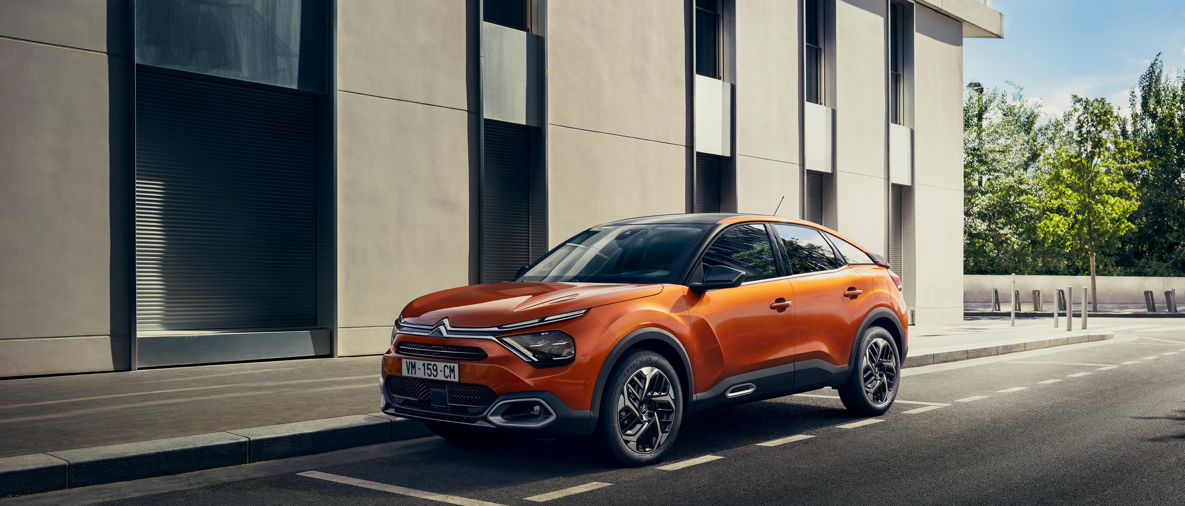 An orange Citroen C4 parked on the side of the road next to a building