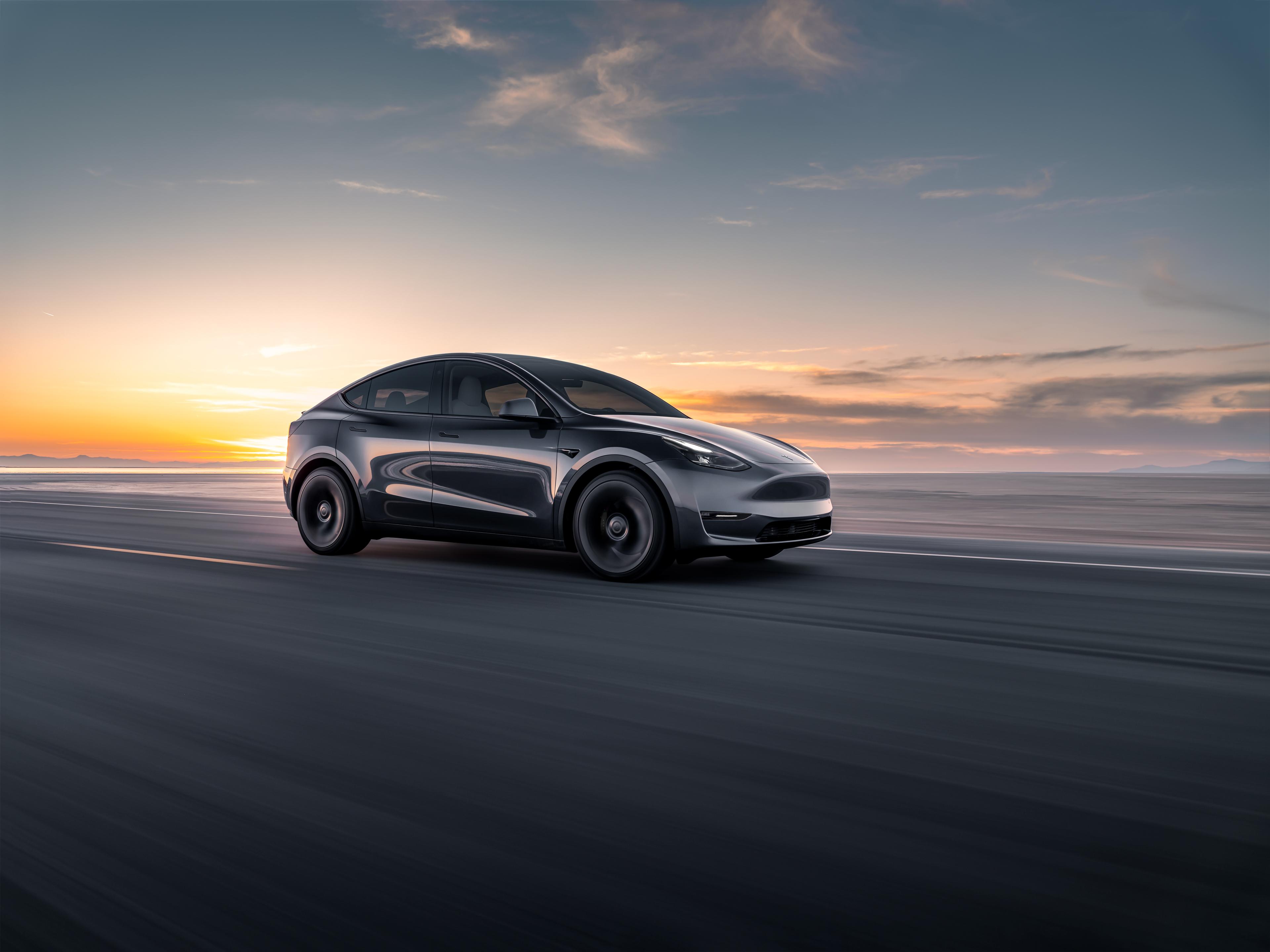 a grey tesla model y driving on a road next to the sea