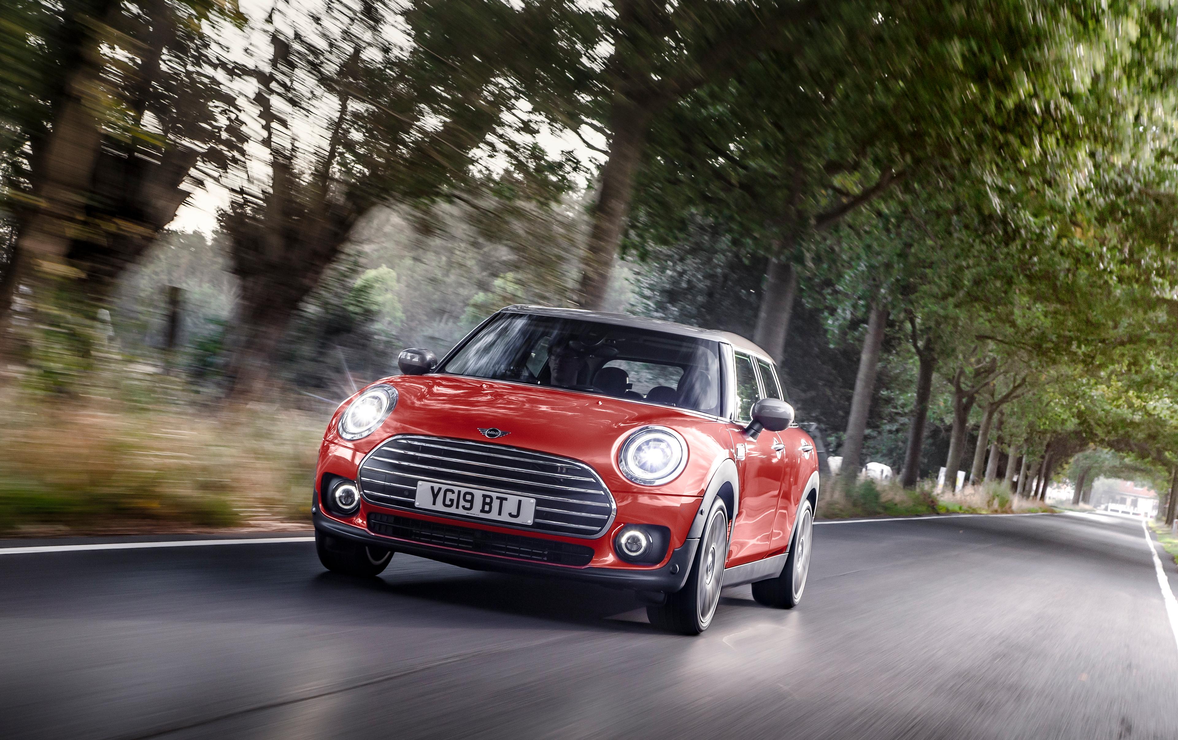 an orange mini clubman driving on a country road through a tree tunnel