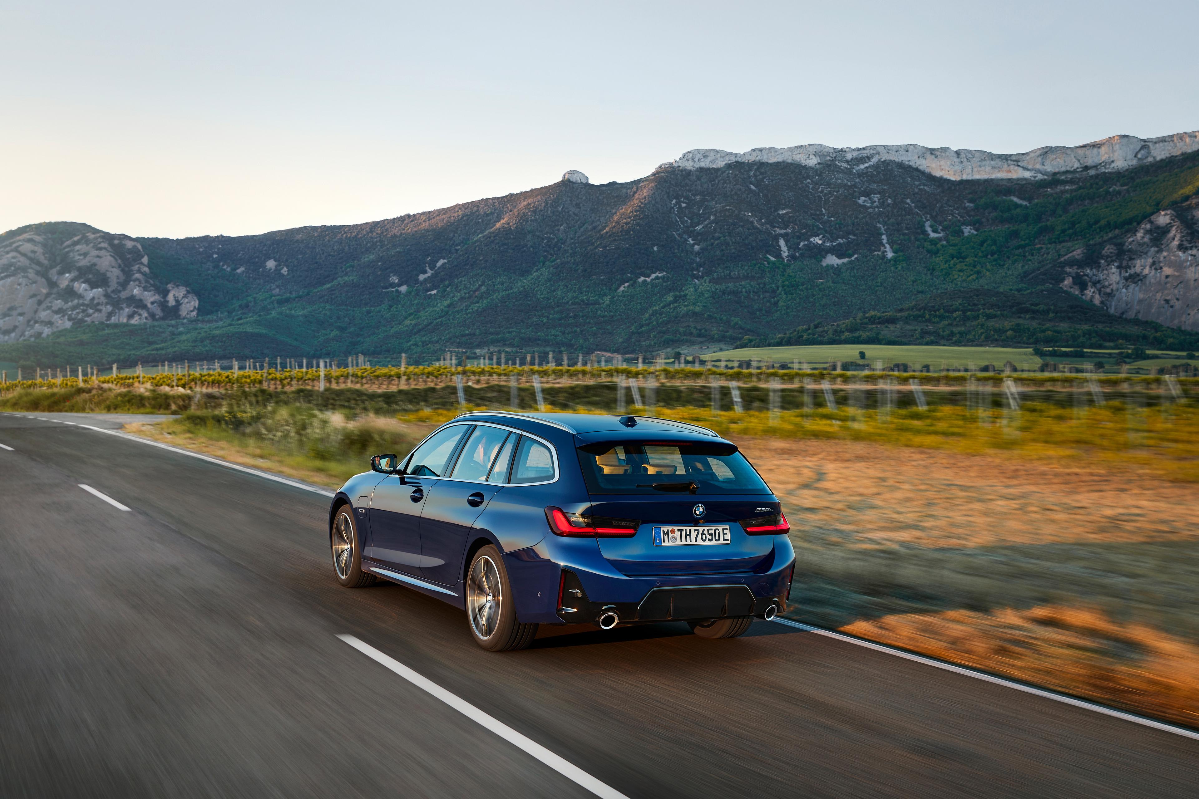 A blue BMW 330e Touring driving in the countryside, showing rear 