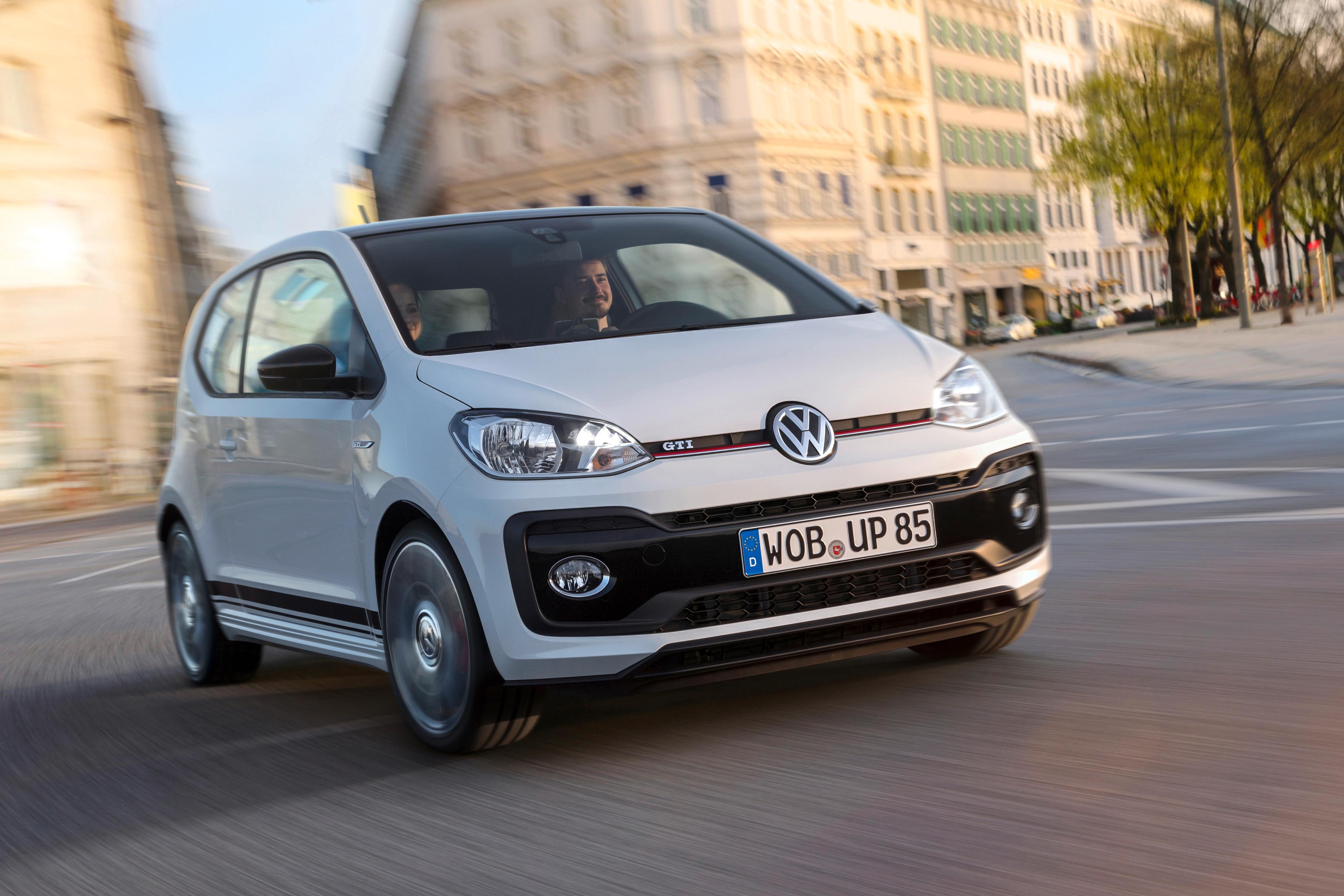 a white vw up gti driving through a town