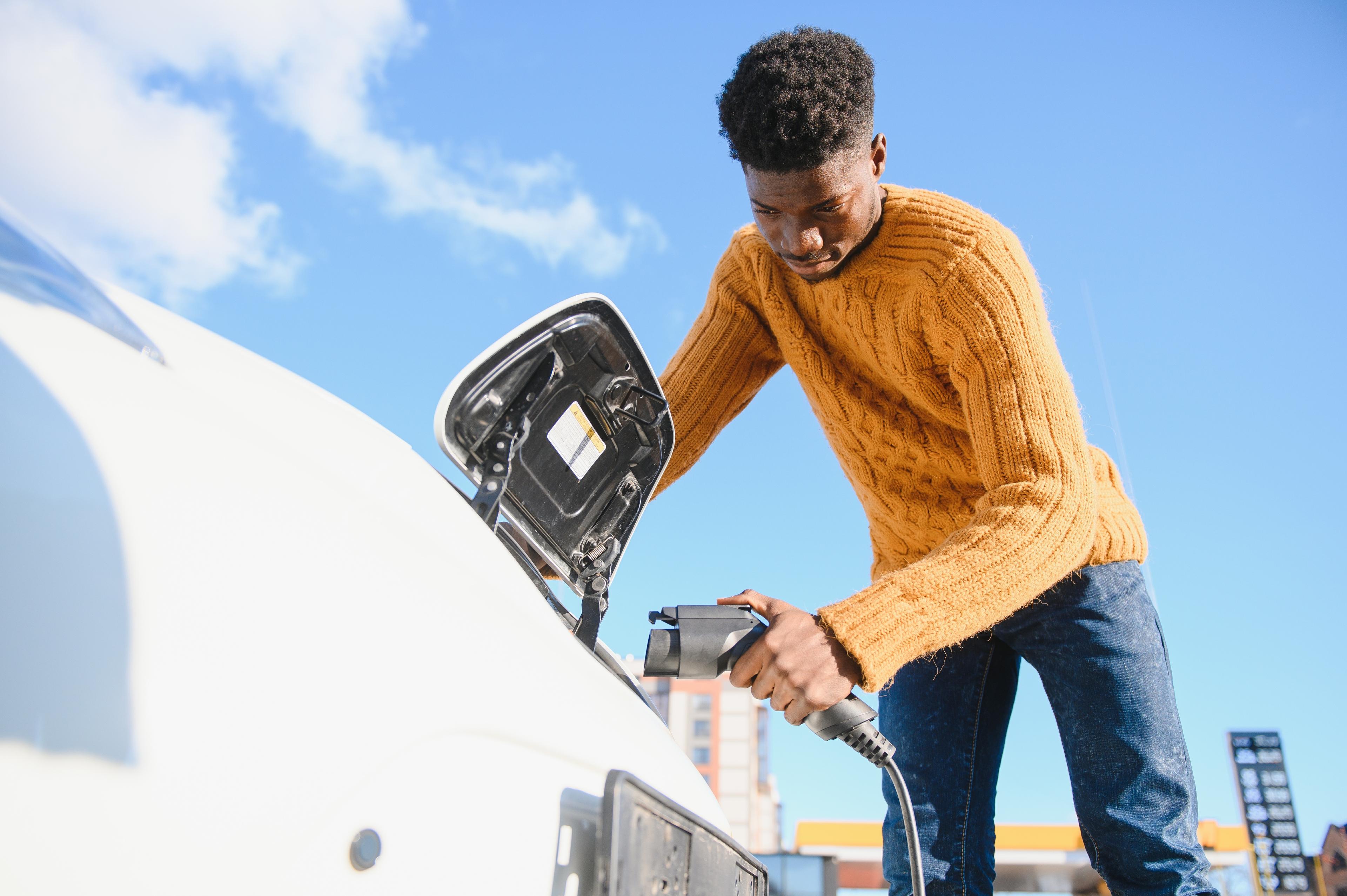 An image showing a man in a yellow jumper charging up an electric car