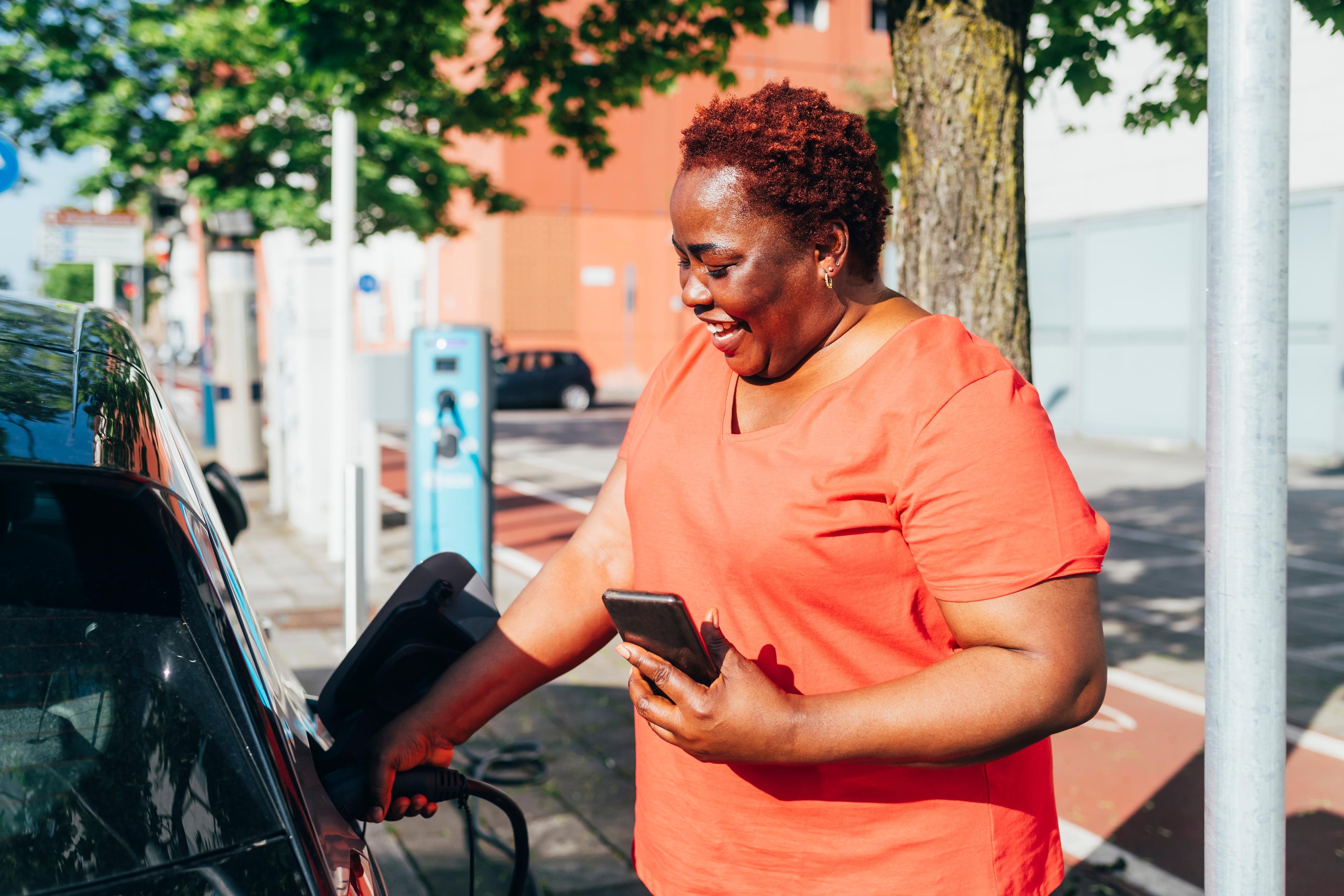 A woman in a red t-shirt plugging in a charger to an electric car