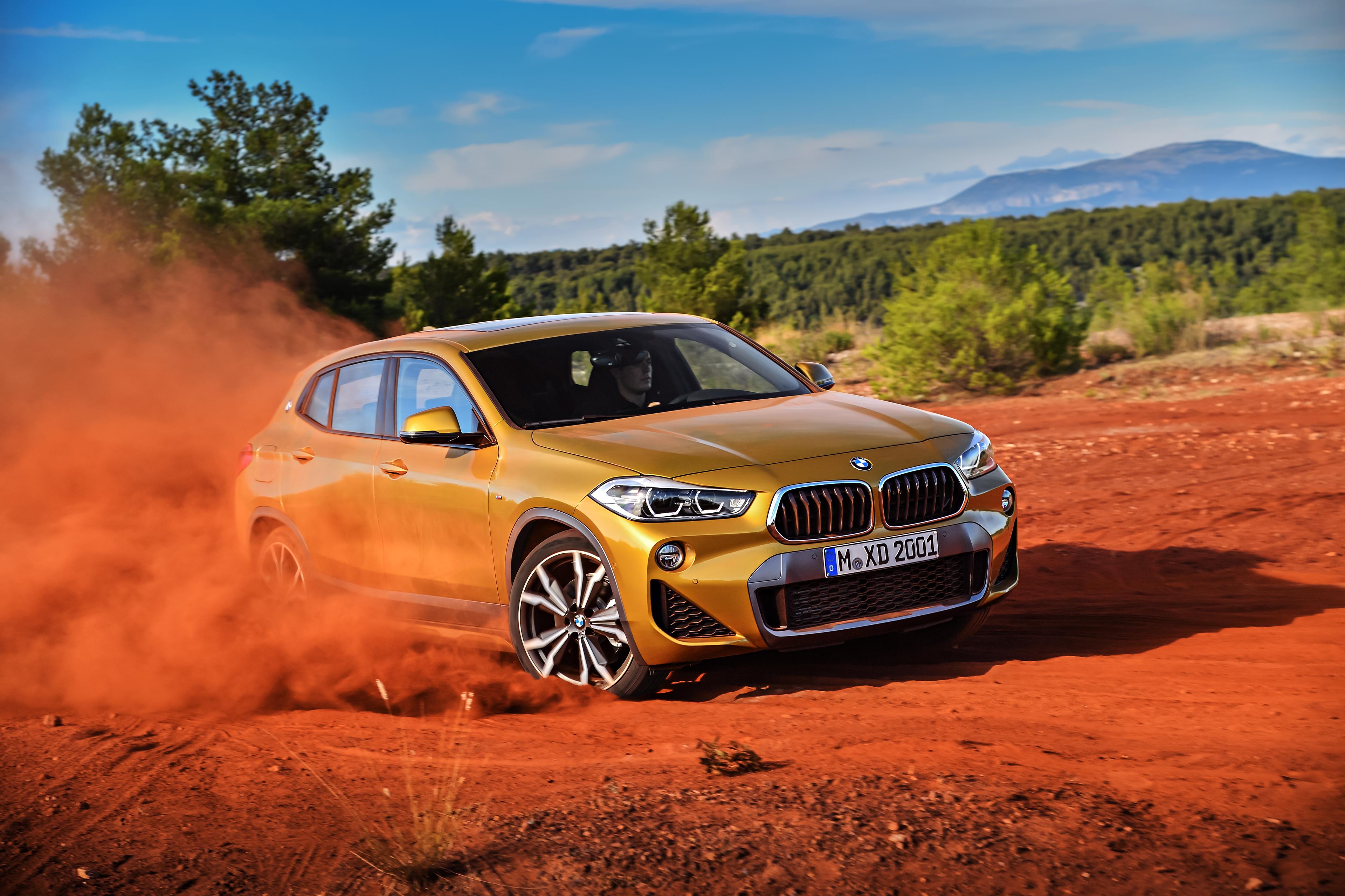 A gold BMW X2 drifting in orange sand