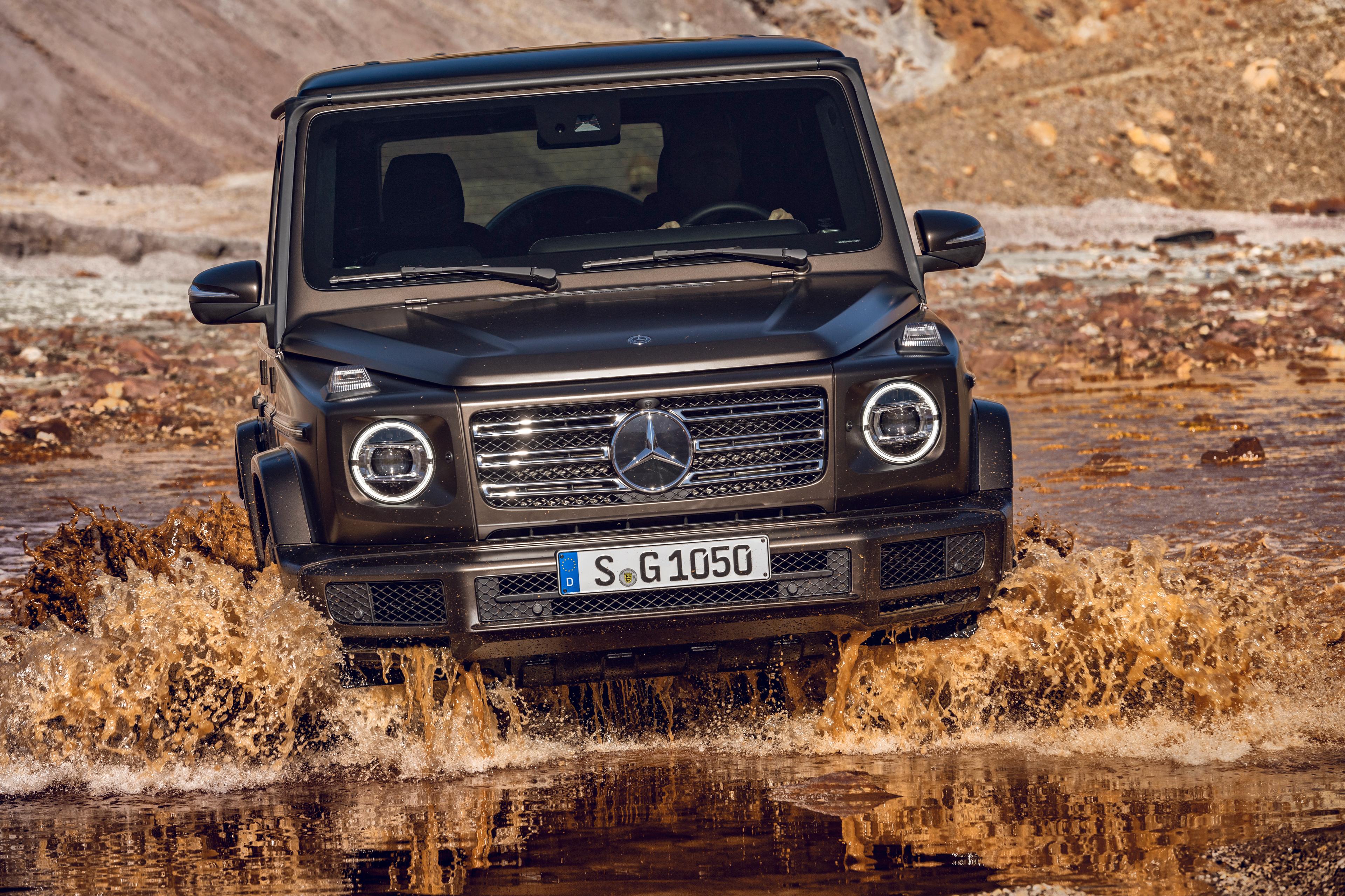 a dark brown mercedes g-class off-roading through water
