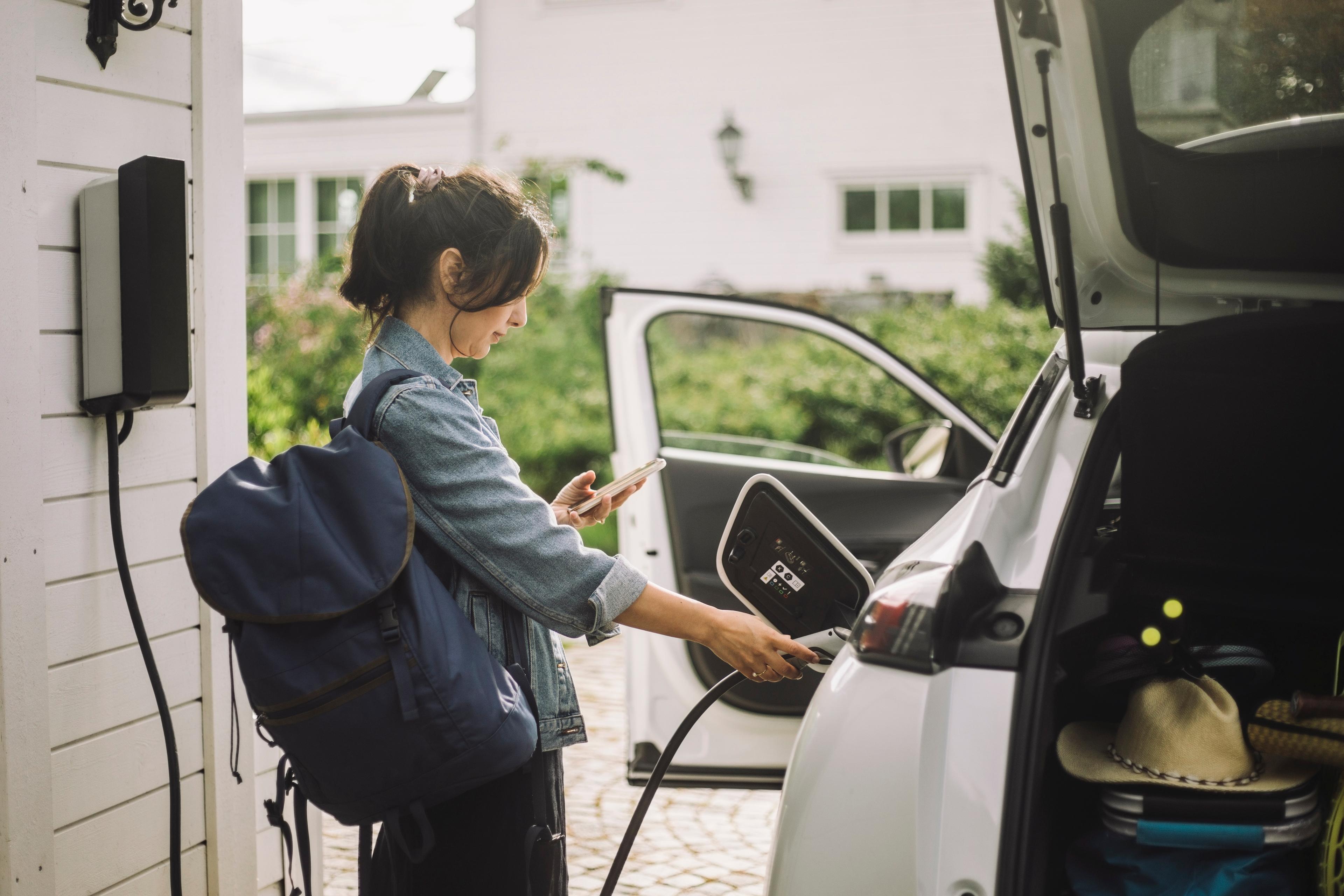 A woman plugging in an EV charger while looking at a phone