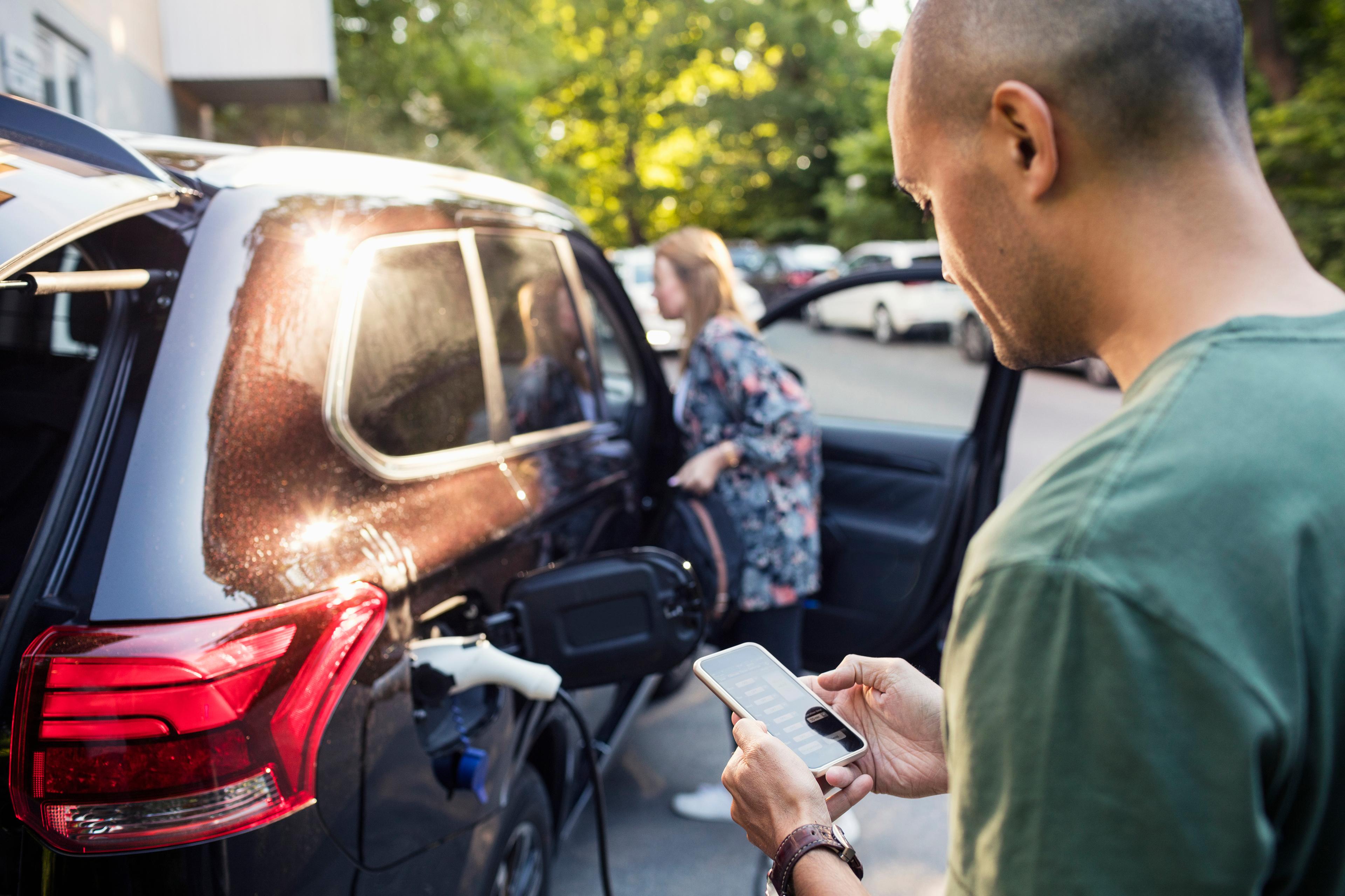 a man stood looking at his hybrid mitsubishi and looking at his phone to monitor the state of charge