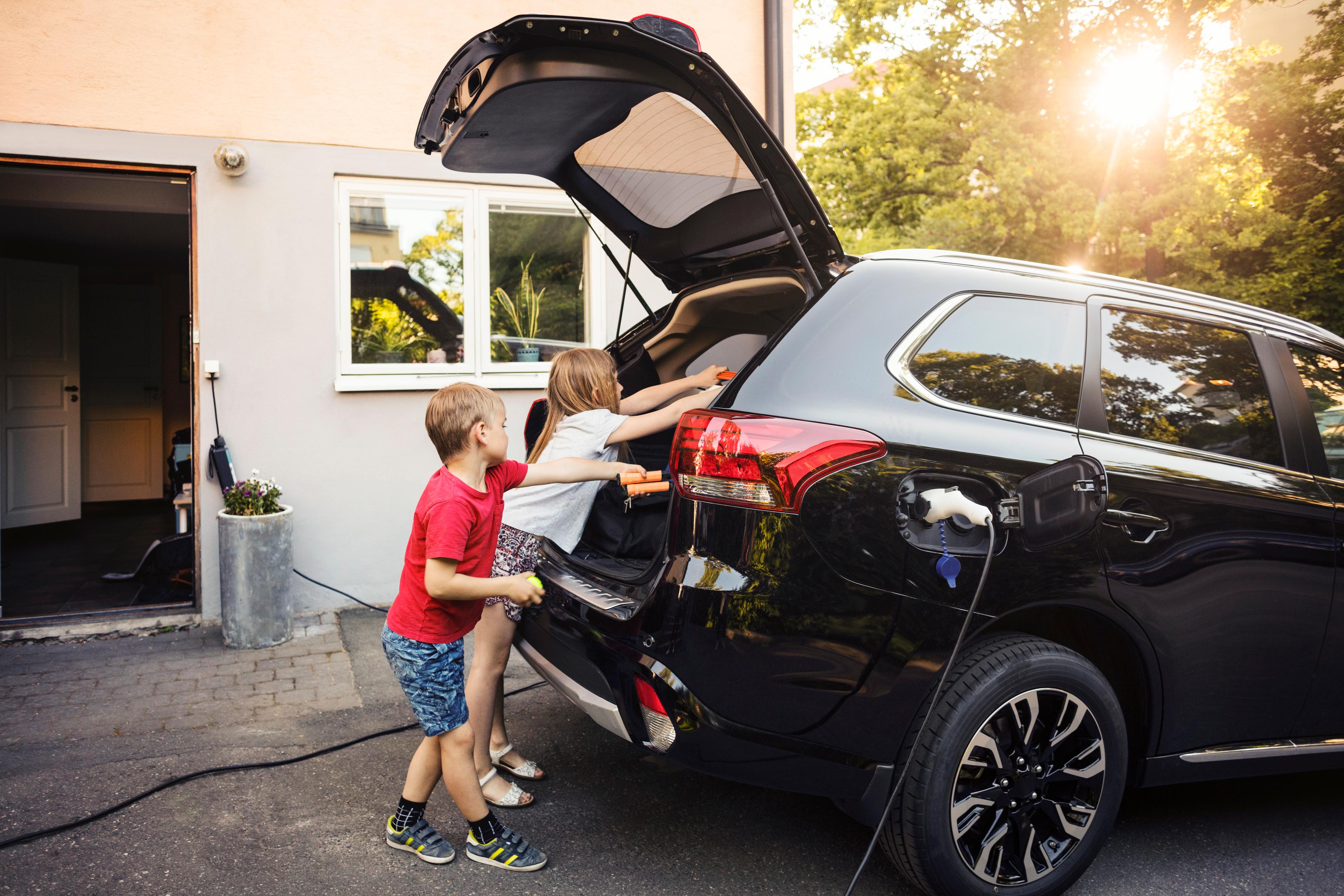 a black mitsubishi hybrid car charging at hone while two kids get toys out of the boot