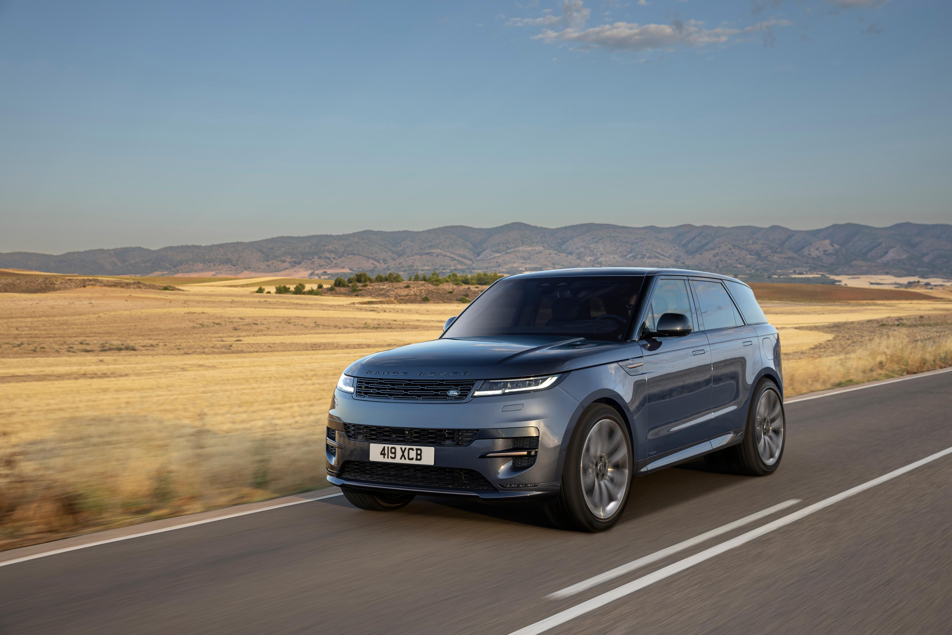 a grey Range Rover Sport driving on a road next to a field