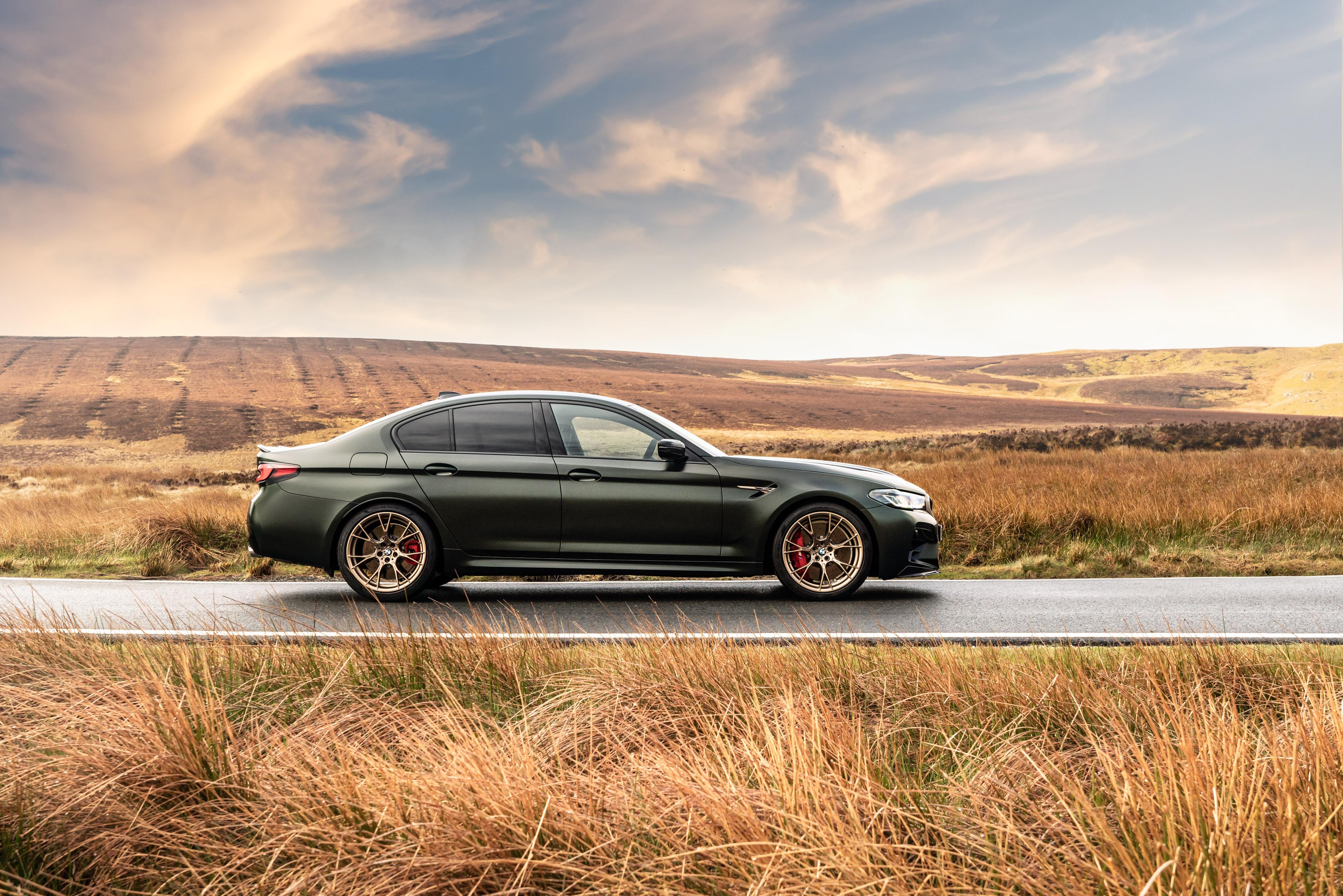 A green BMW M5 driving near fields