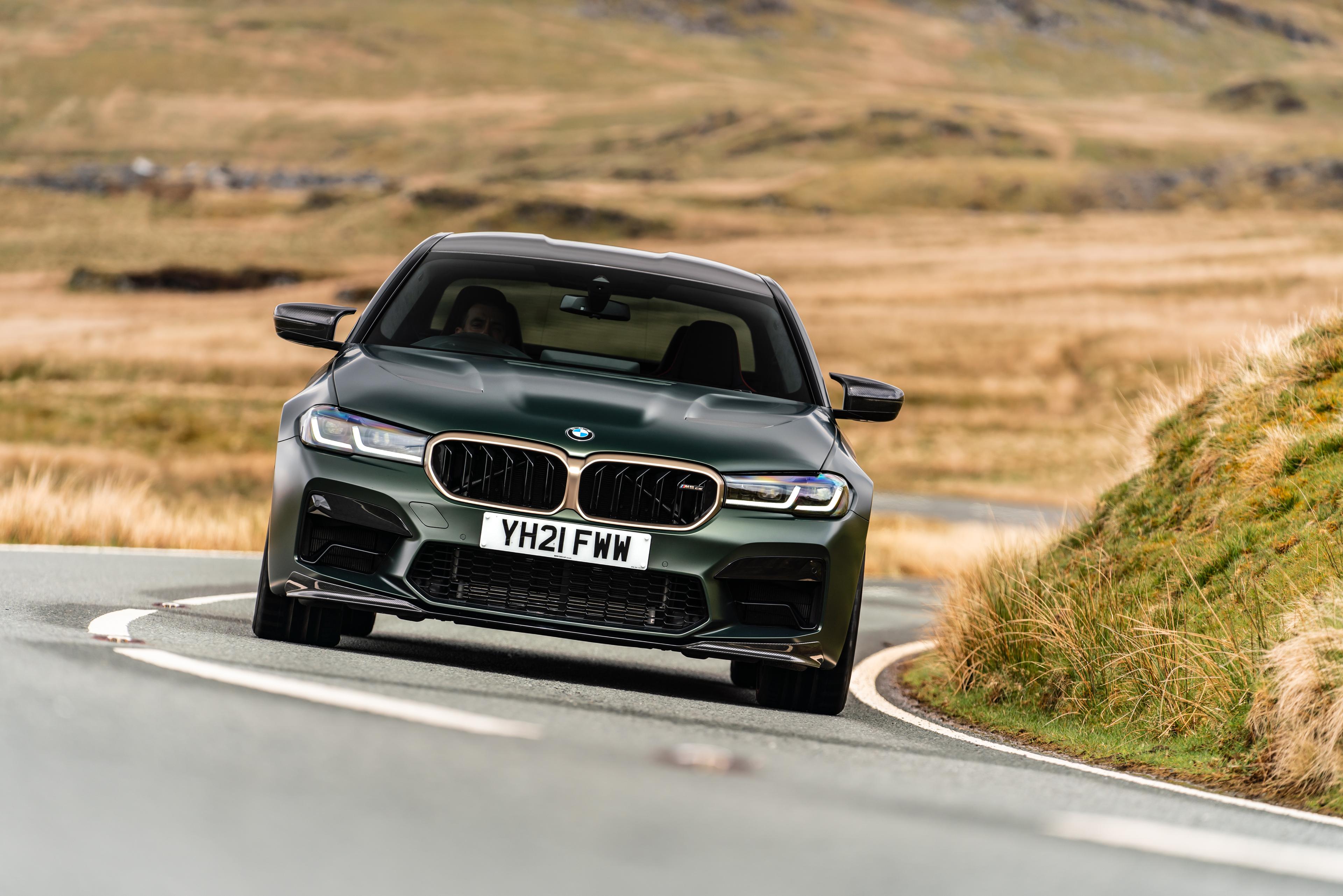 a dark green and gold BMW M5 driving on a countryside road in britain