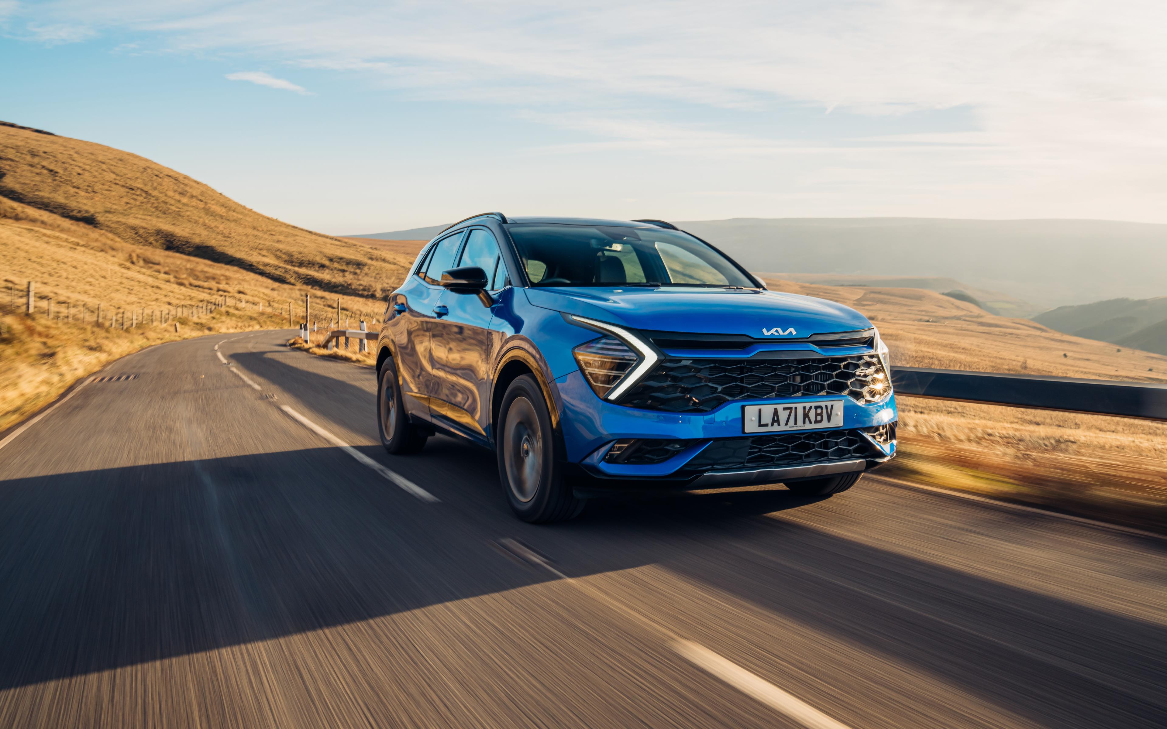 A blue Kia Sportage driving along a road with hills in the background